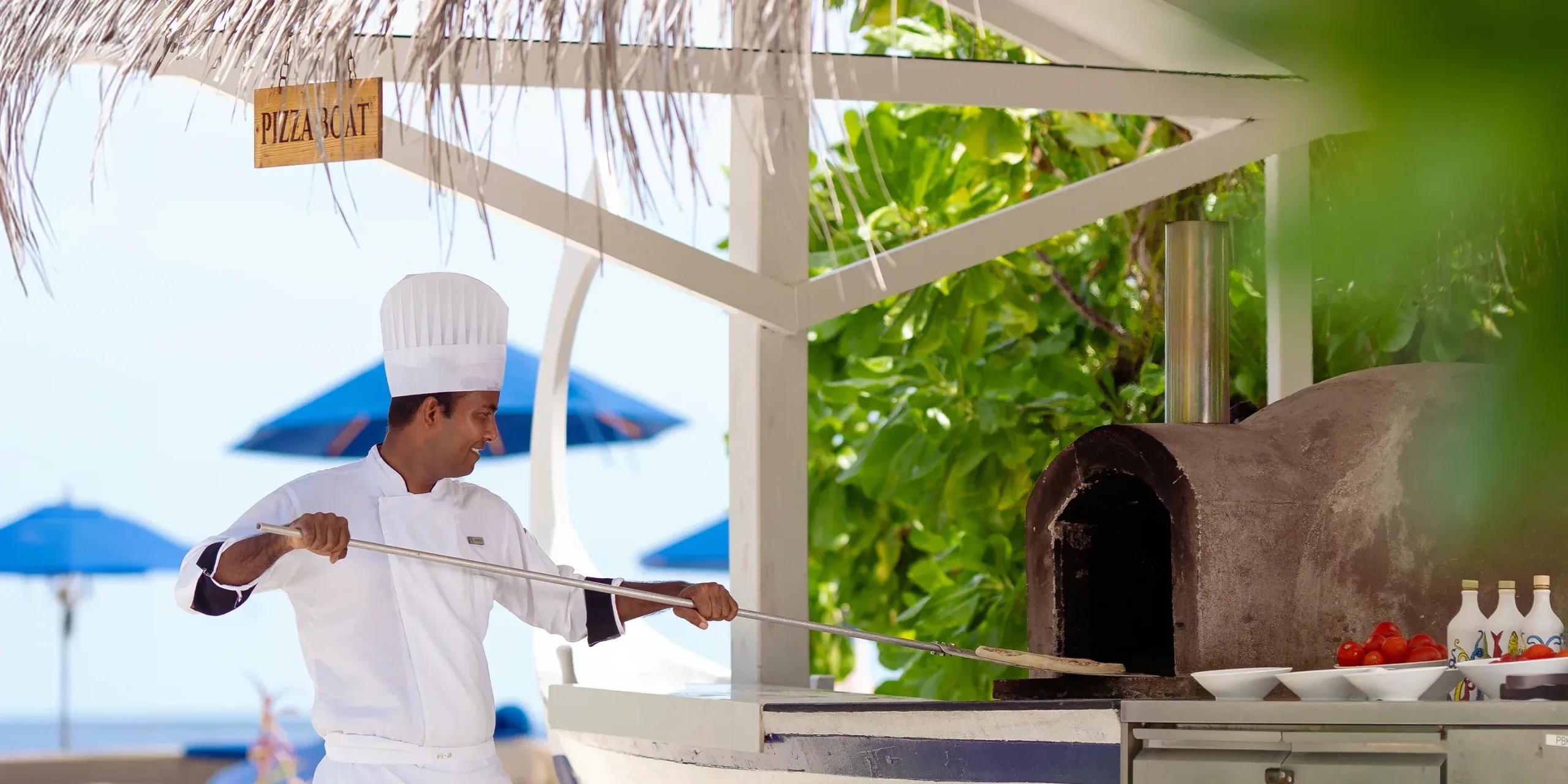 A chef sliding a pizza into Pizza Boat's purpose-built wood-fired oven at Baglioni Maldives
