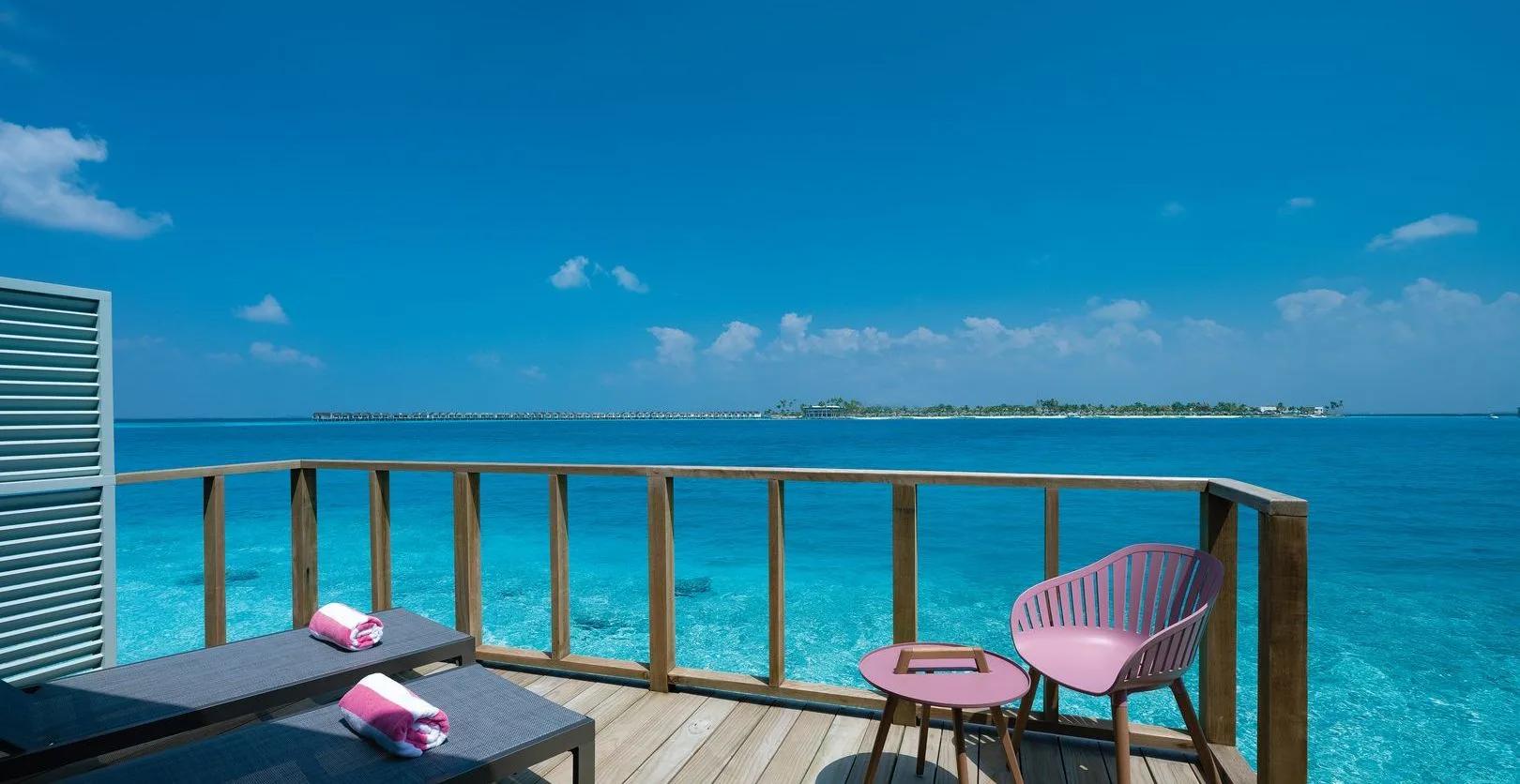 Loungers on an overwater villa deck at OBLU SELECT Lobigili, looking back along the jetty toward the island and its own villa row