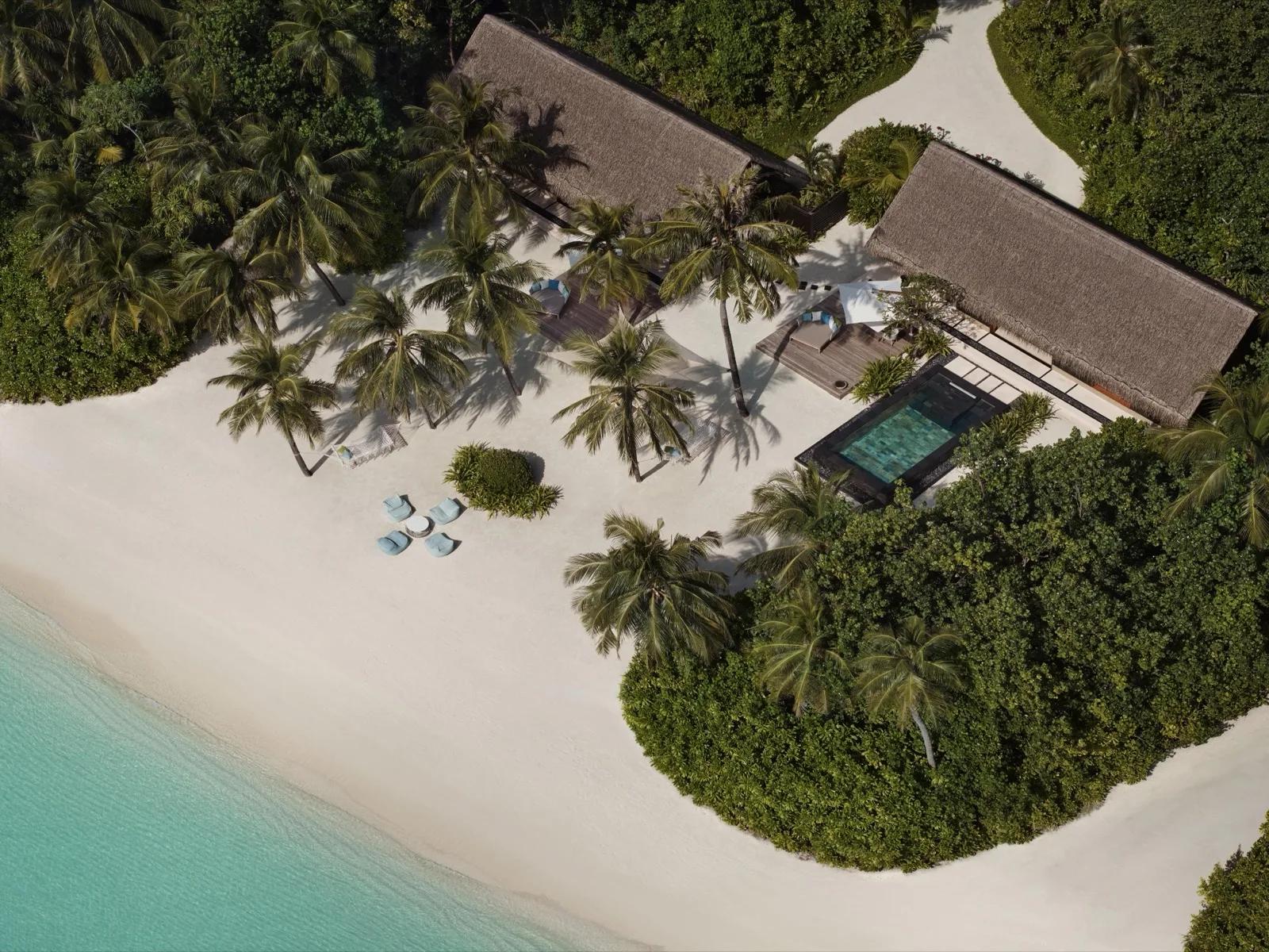 Aerial view of a Two-Villa Residence at One&Only Reethi Rah, two adjoining thatched-roof villas sharing one pool deck on the beach
