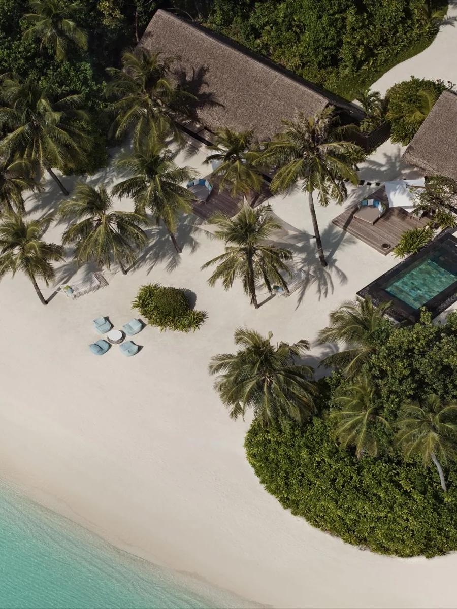 Aerial view of a Two-Villa Residence at One&Only Reethi Rah, two adjoining thatched-roof villas sharing one pool deck on the beach