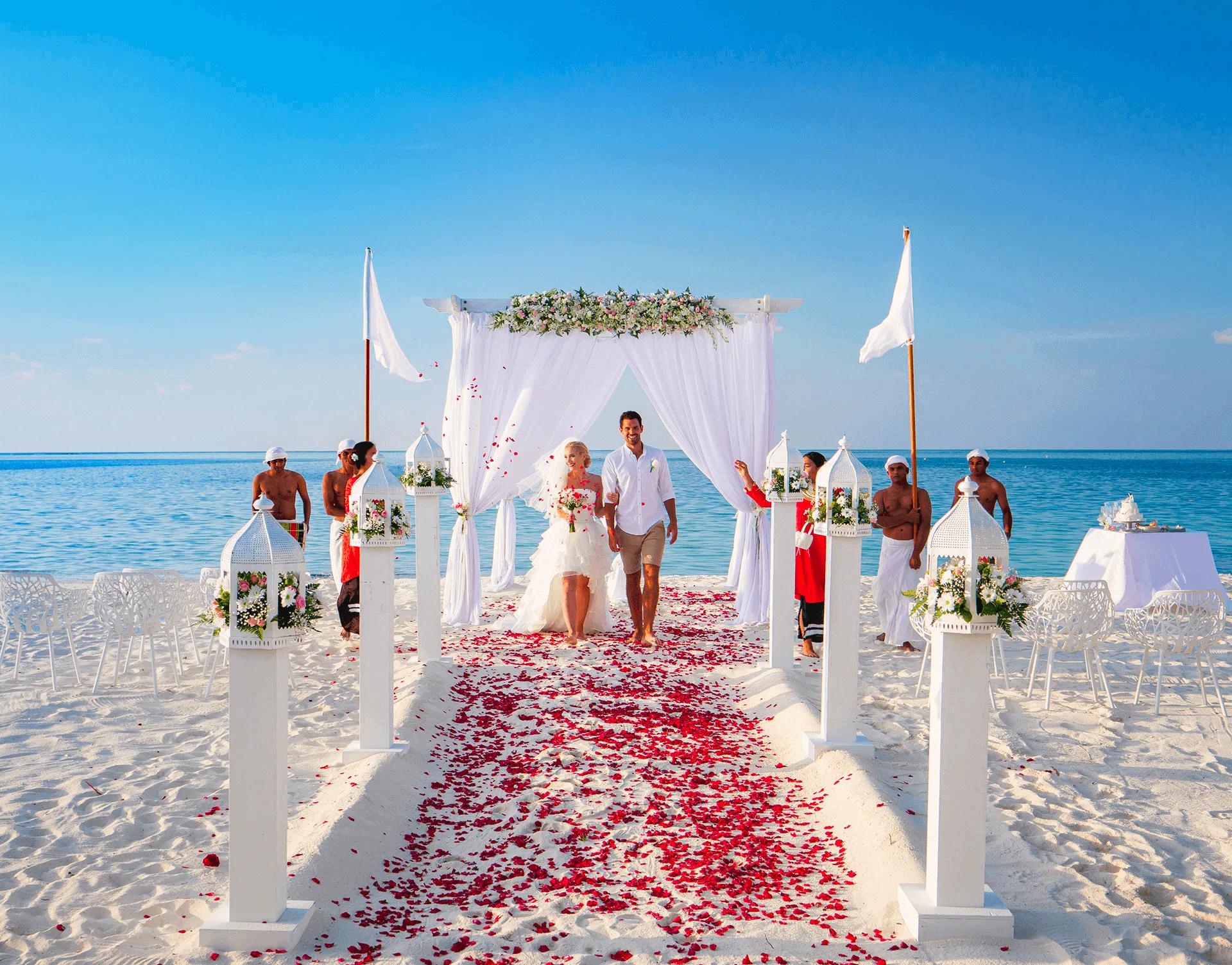 A couple walking up a petal-strewn aisle on the beach after their wedding ceremony