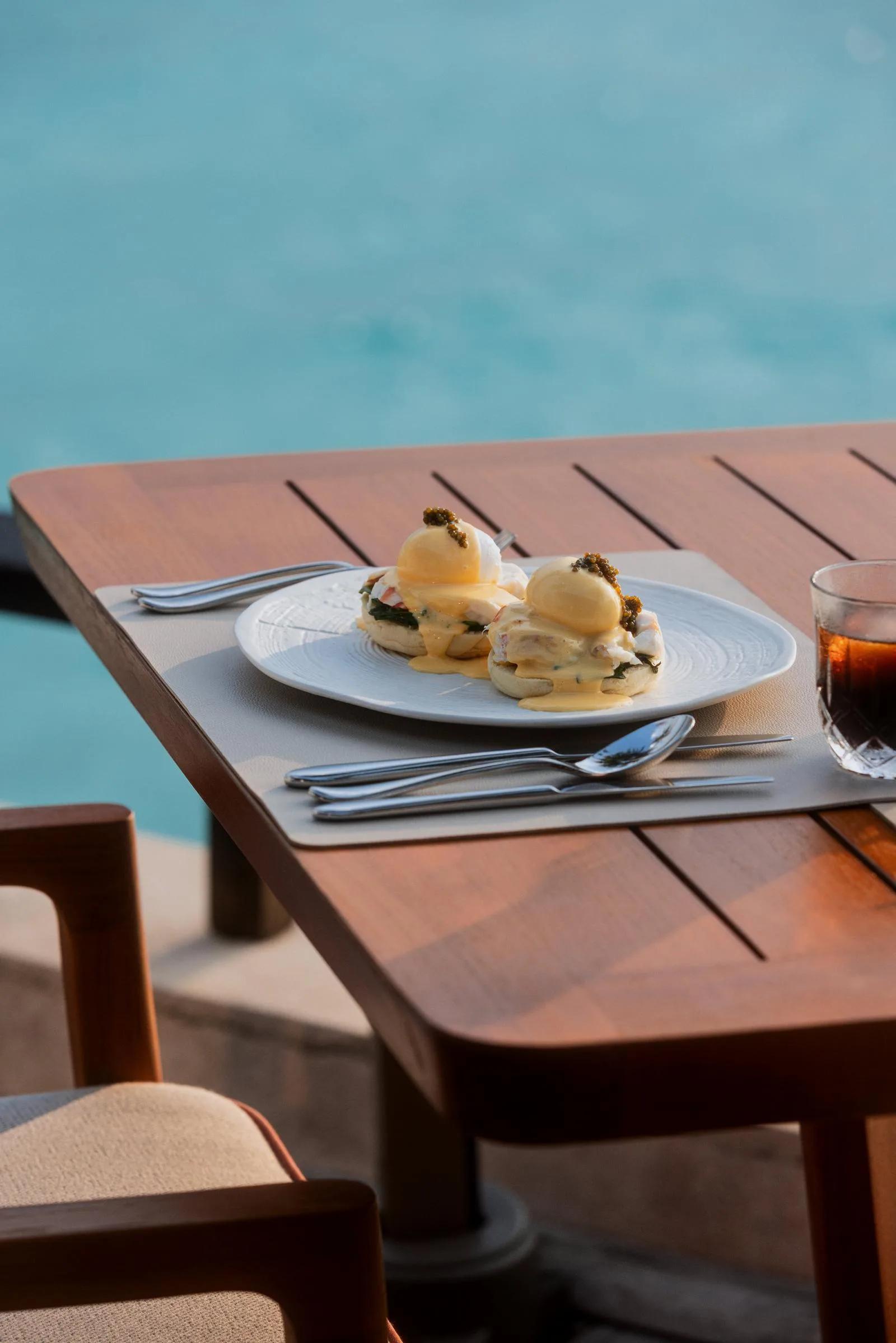 A plated dish and an iced drink beside a pool at One&Only Reethi Rah — standing in for Beach Club, the resort's casual beachside restaurant, since no dedicated Beach Club photograph was collected