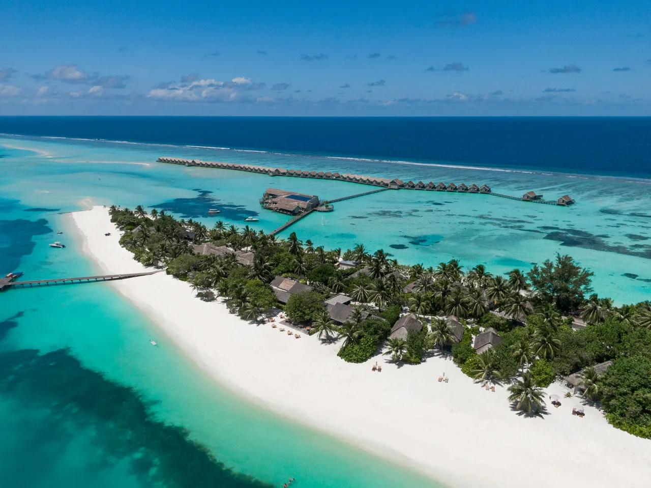 Aerial view of LUX* South Ari Atoll showing its sandy beach, palm-covered island and overwater villa jetty reaching to the reef