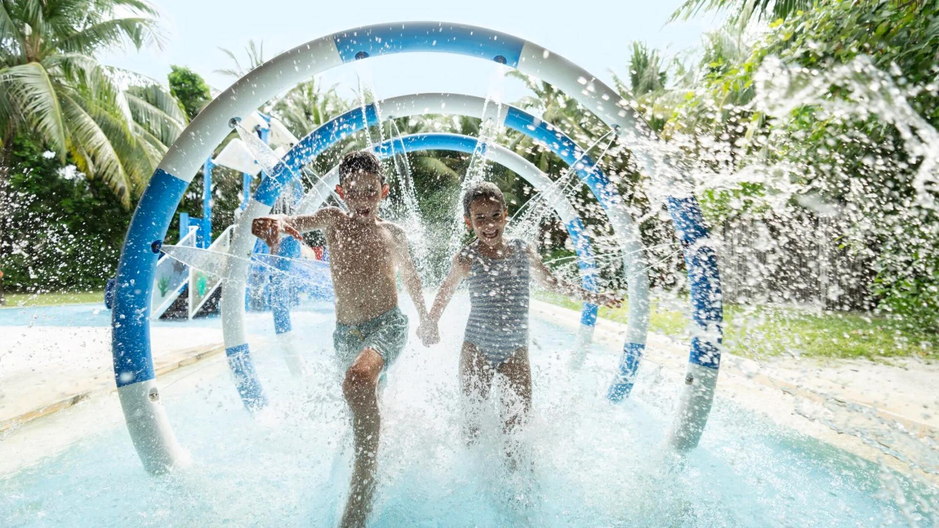 Two children running through a water-jet archway at the Planet Trekkers splash pool