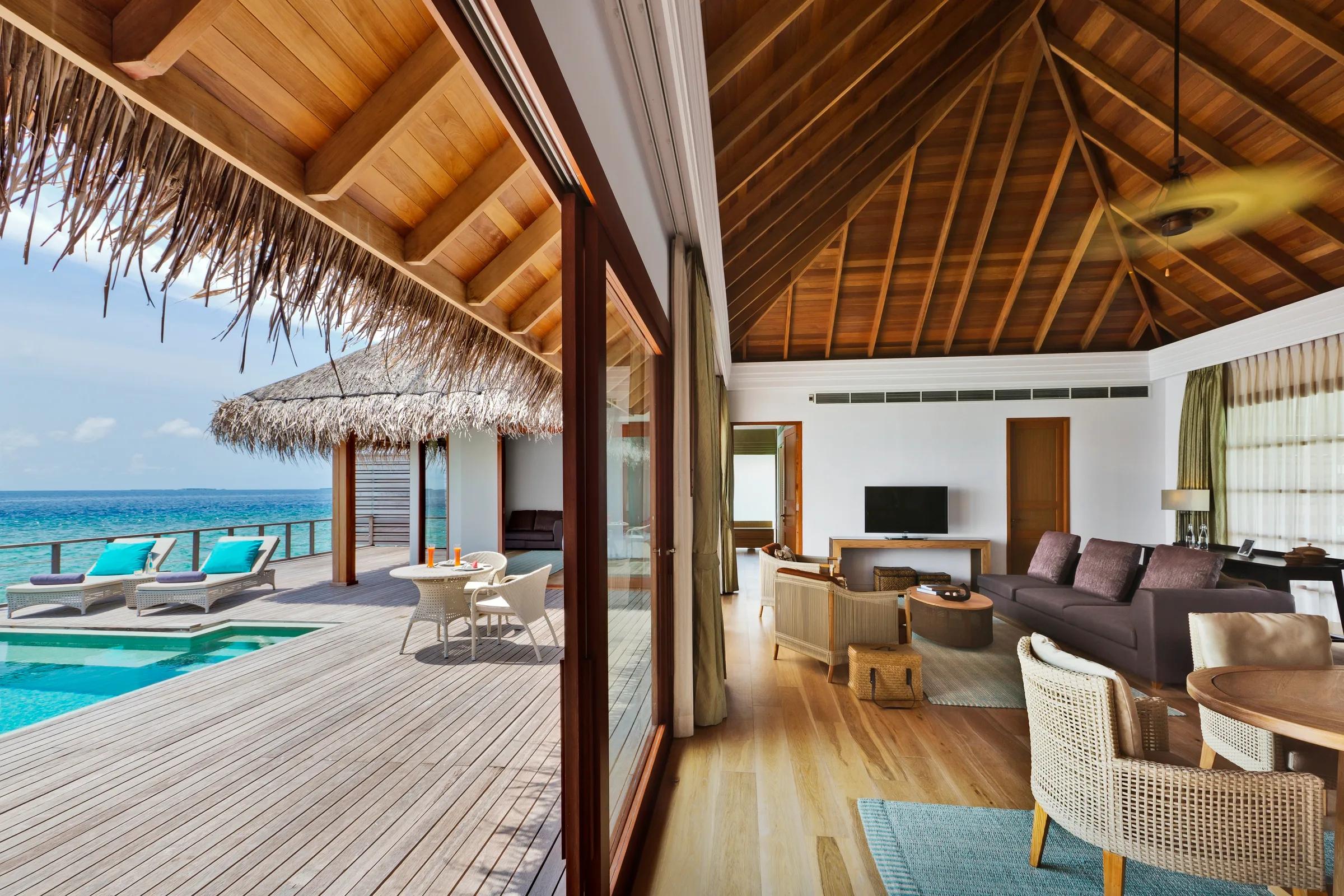 The open-plan living room and deck of a Two Bedrooms Overwater Pool Pavilion at Dusit Thani Maldives, glass doors open to the lagoon