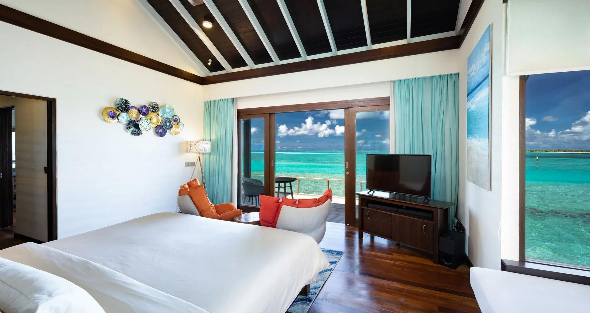 A Water Villa's bedroom, reef-life wall art beside sliding doors onto the deck above the lagoon