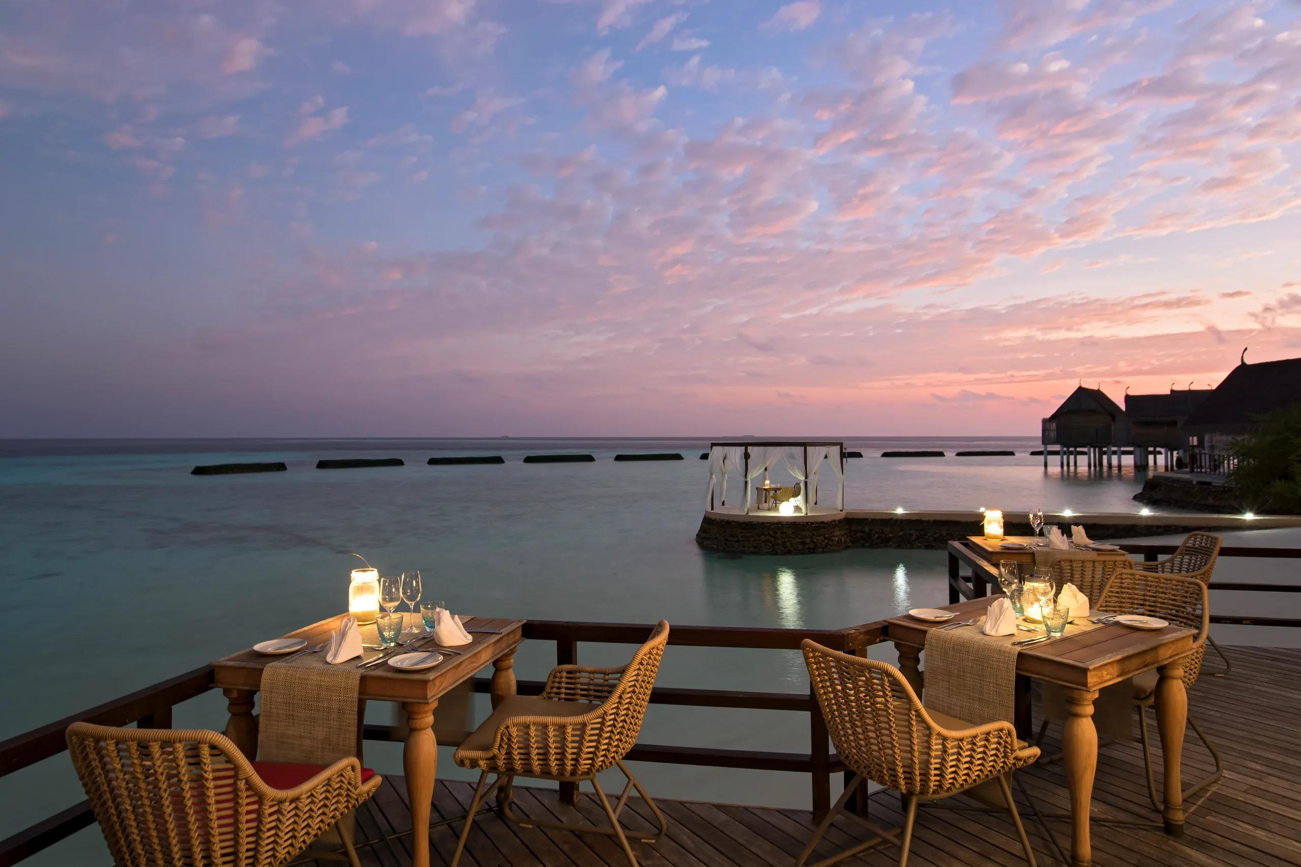 Manta Restaurant's over-water dining extension set for dinner at dusk, tables lit by lantern beside the lagoon
