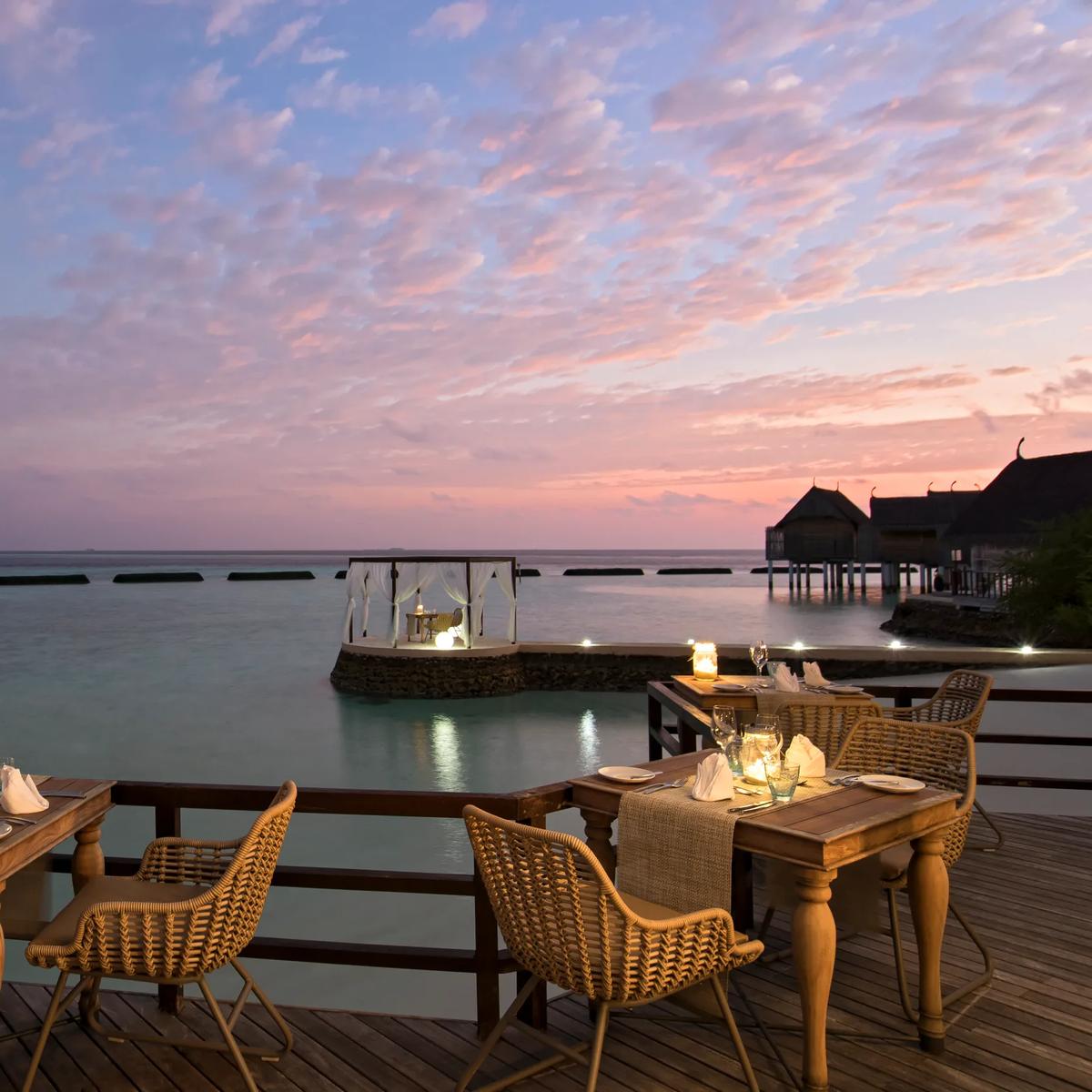 Manta Restaurant's over-water dining extension set for dinner at dusk, tables lit by lantern beside the lagoon