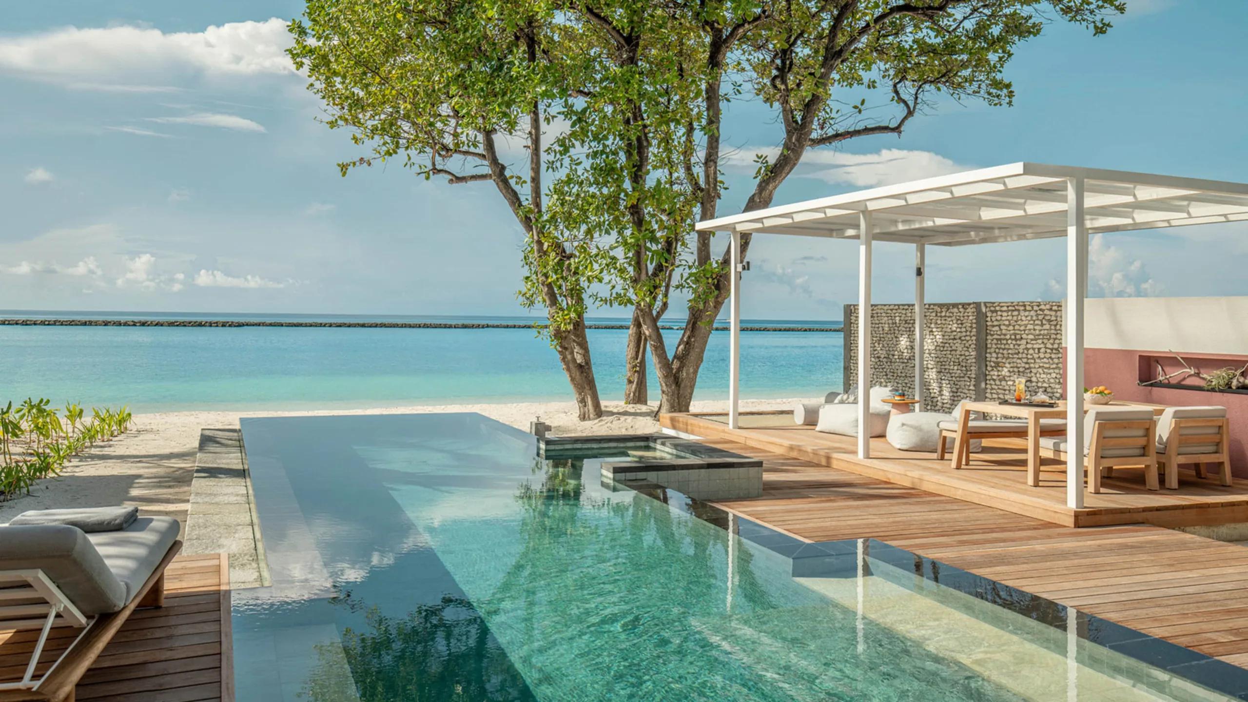 A Premier Oceanfront Bungalow's pool running toward the beach beneath large shade trees, with a dining cabana alongside