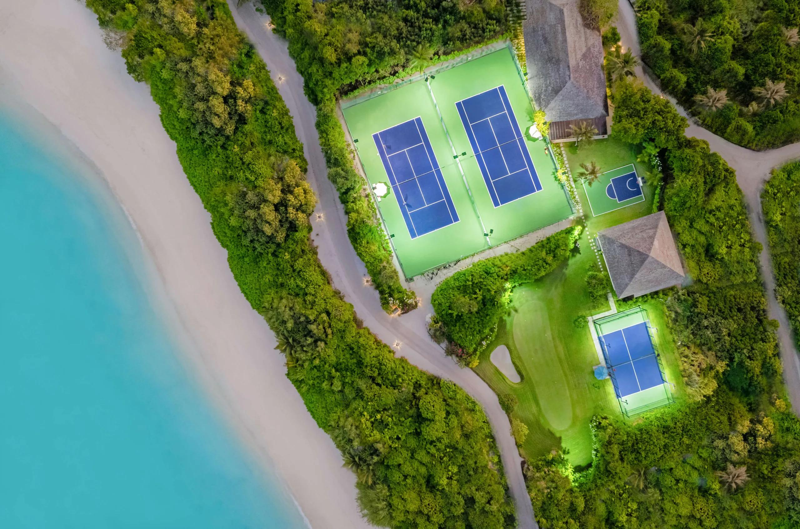 Aerial view of Hideaway's floodlit tennis and padel courts beside the beach