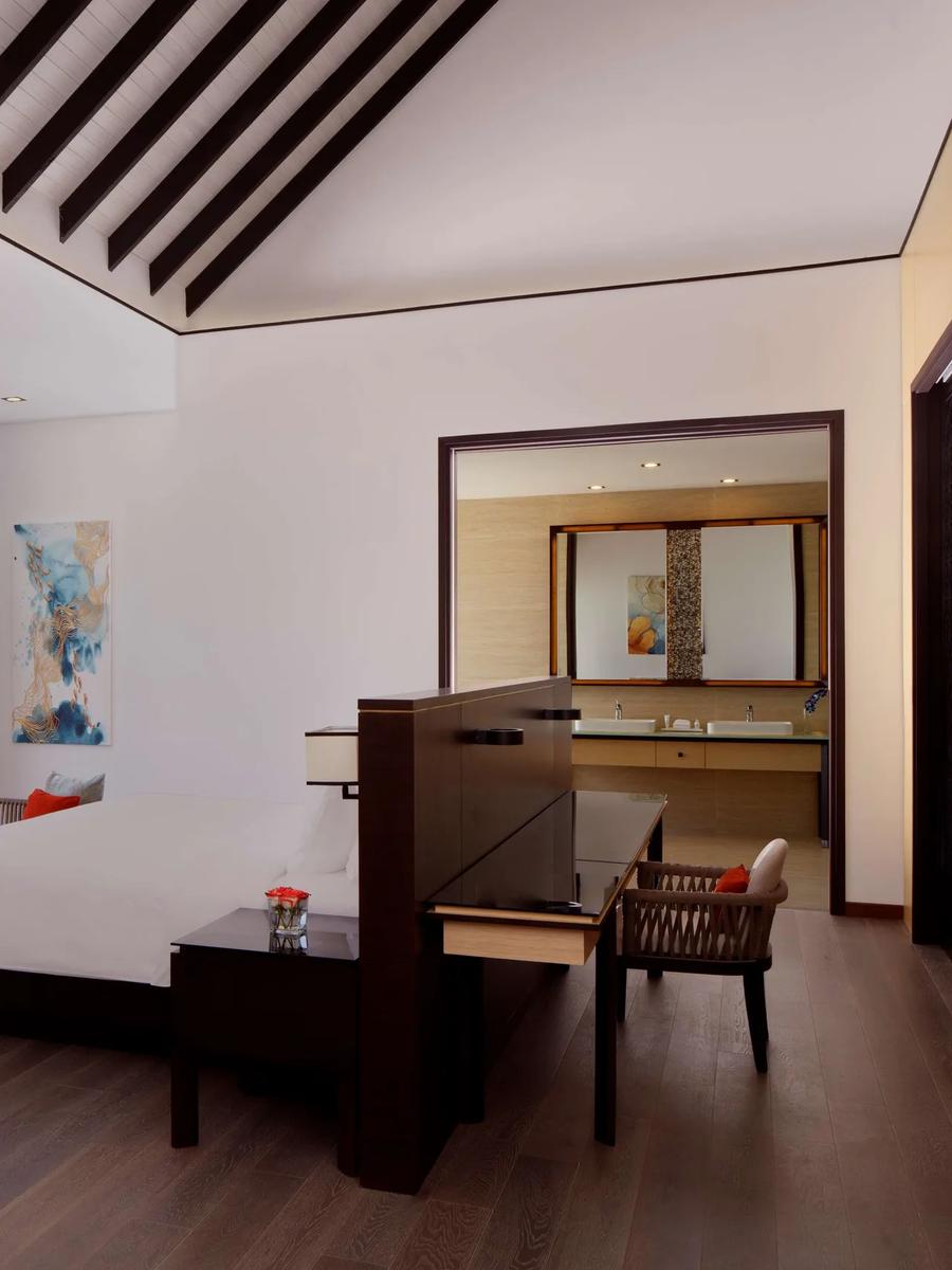 The bedroom of an Overwater Villa at Radisson Blu Resort Maldives, glass doors open to its private pool deck and the lagoon beyond