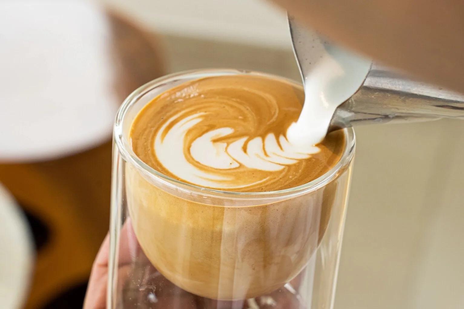 A barista pouring steamed milk into a glass to finish latte art at Café Lounge