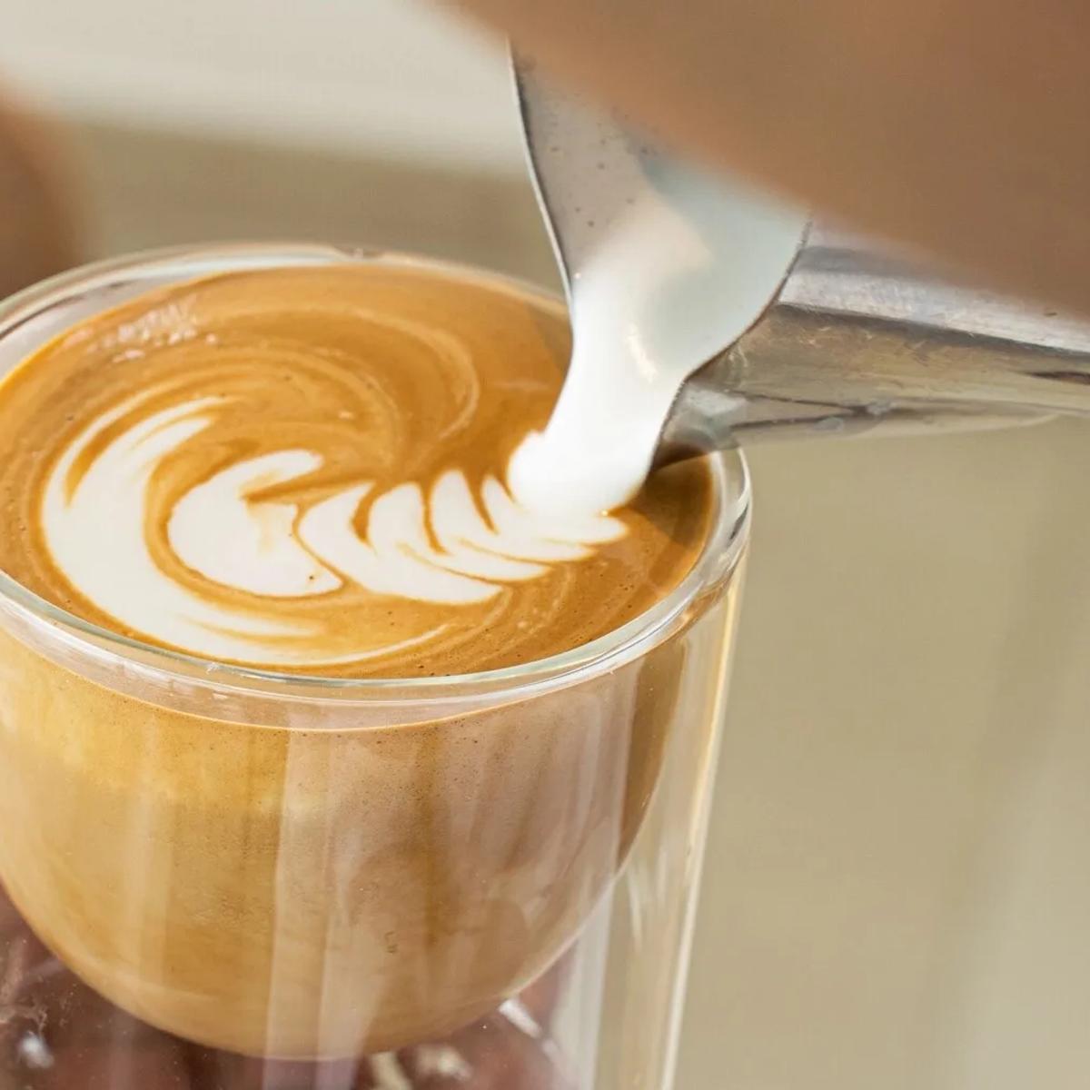A barista pouring steamed milk into a glass to finish latte art at Café Lounge