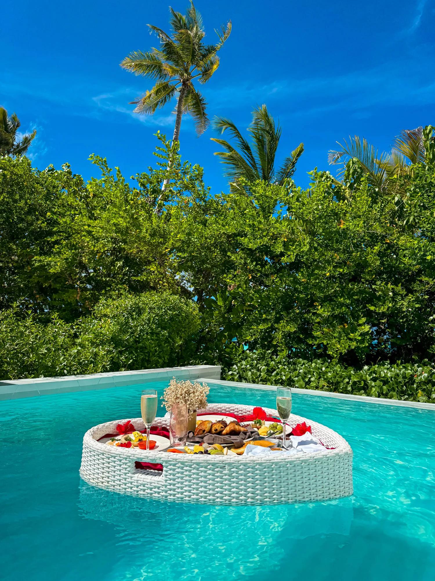 A breakfast tray with champagne and pastries set afloat on a Beach Suite Pool's private pool, palm trees overhead