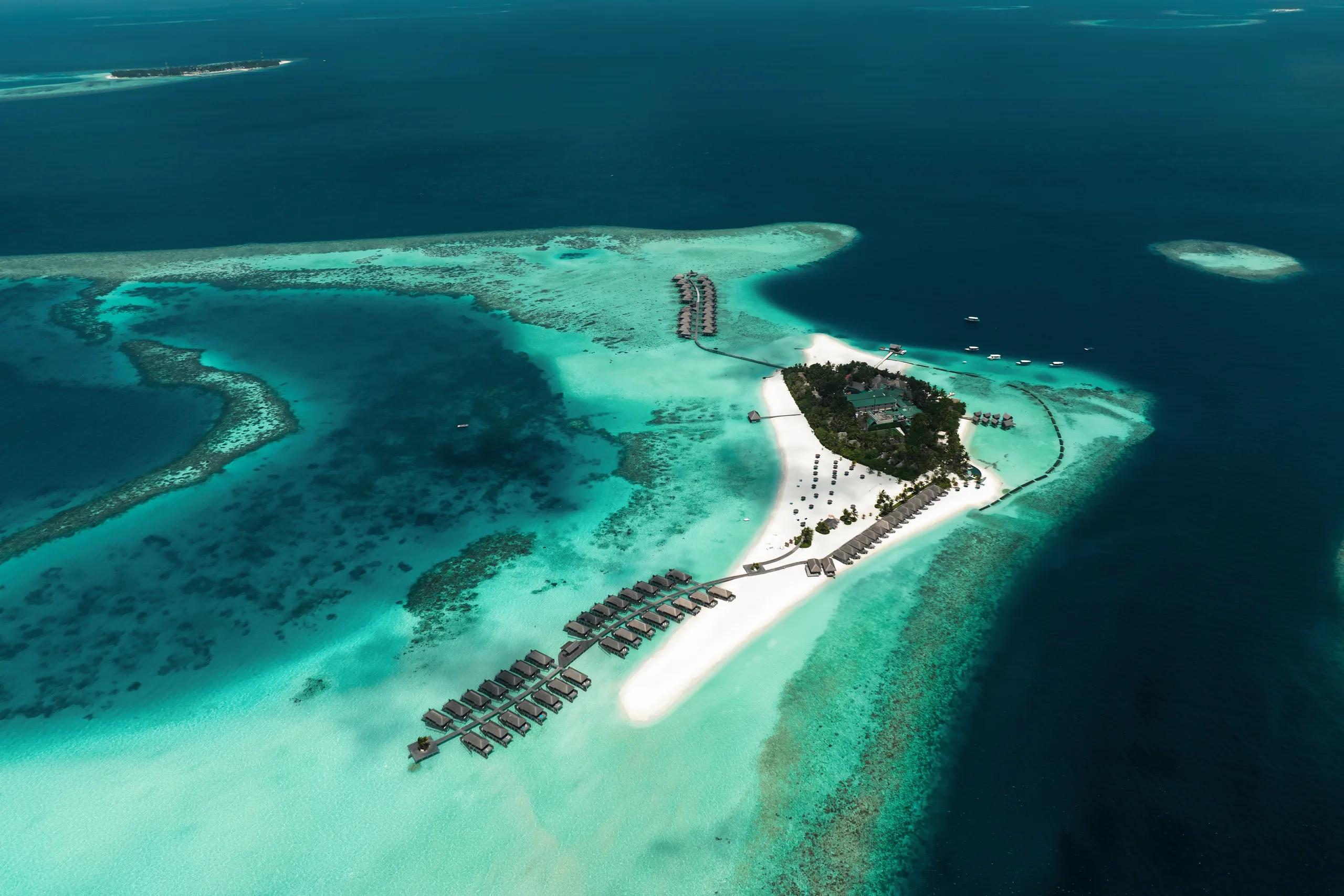 Aerial view of Constance Moofushi's triangular island, its beach and water villa jetties reaching into the South Ari Atoll lagoon