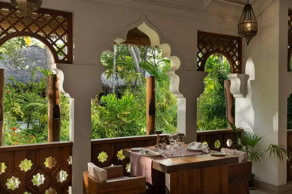Tandoor Mahal's Moorish-arched dining pavilion, a table set for two beneath carved white archways and tropical planting