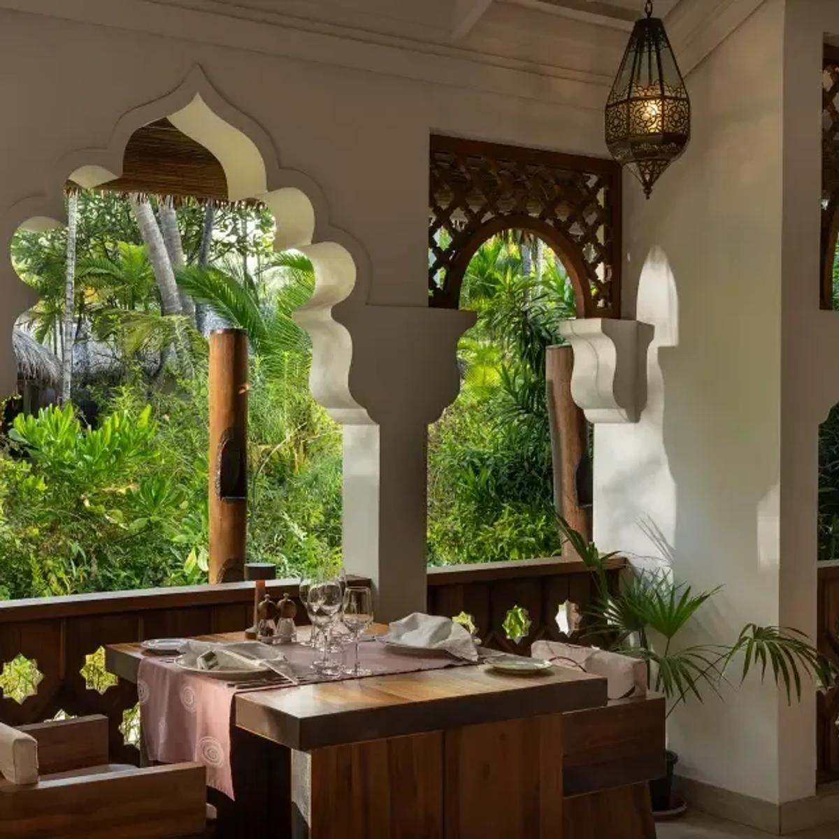 Tandoor Mahal's Moorish-arched dining pavilion, a table set for two beneath carved white archways and tropical planting