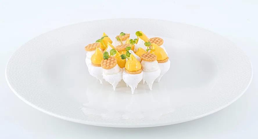 A dessert plate of meringue, mango, and thin golden wafers, plated for in-house dining