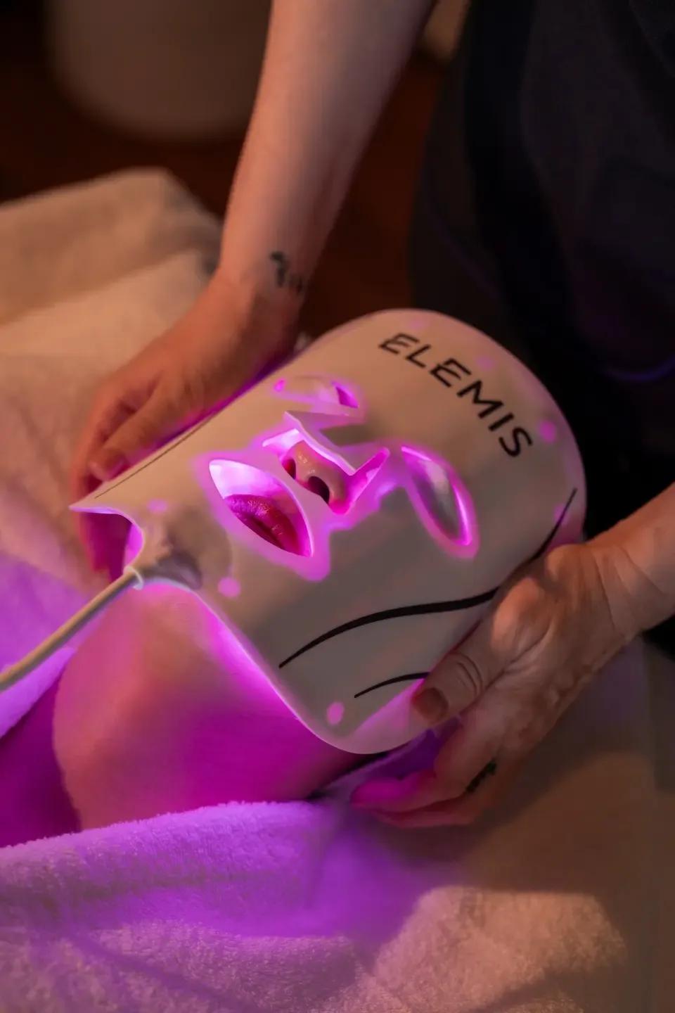 Close-up of an illuminated ELEMIS LED facial mask being fitted to a guest's face during a treatment