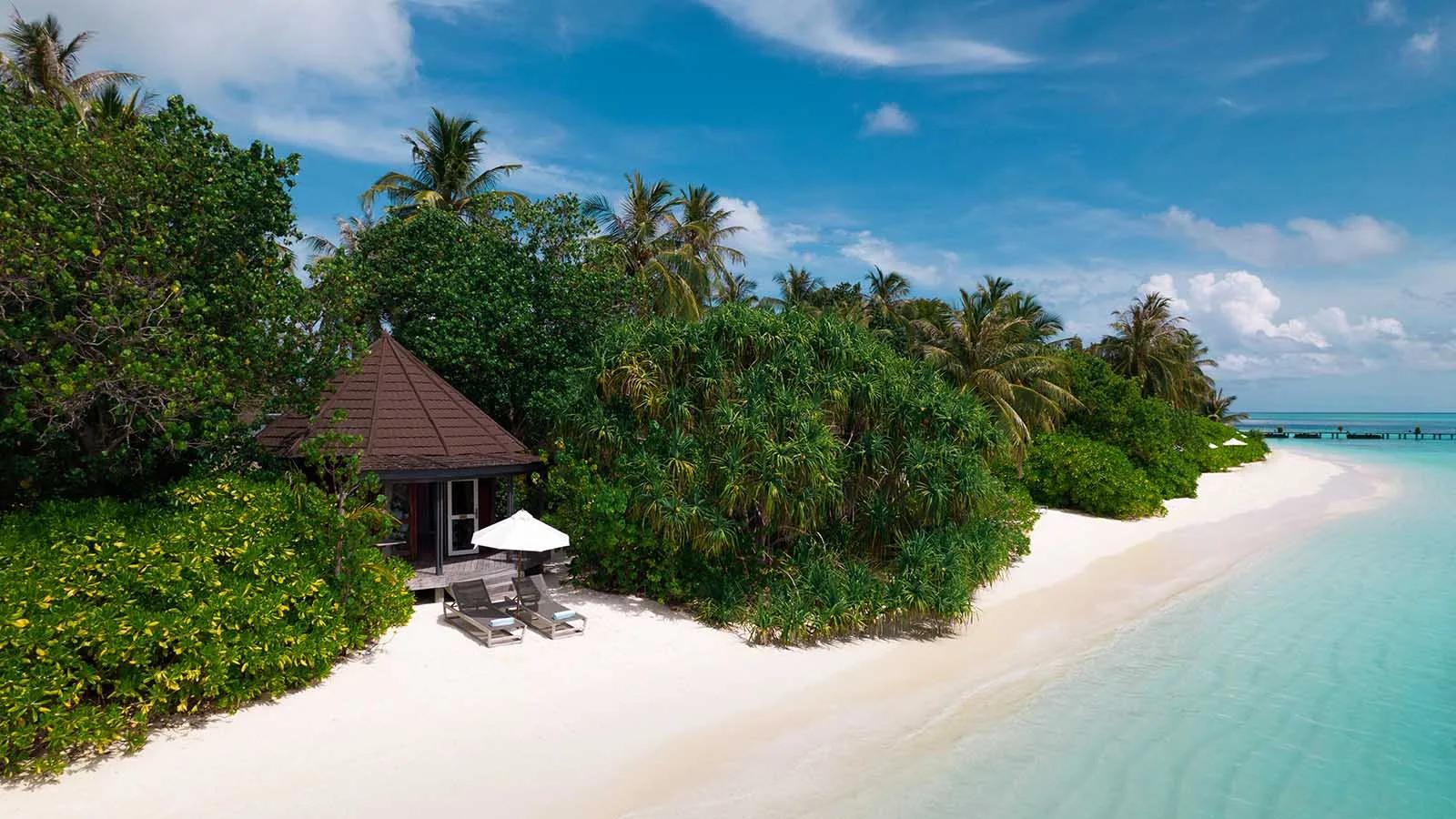 A Beach Villa's thatched roof and porch tucked into the tree line, steps from the beach and a shaded seating area outside