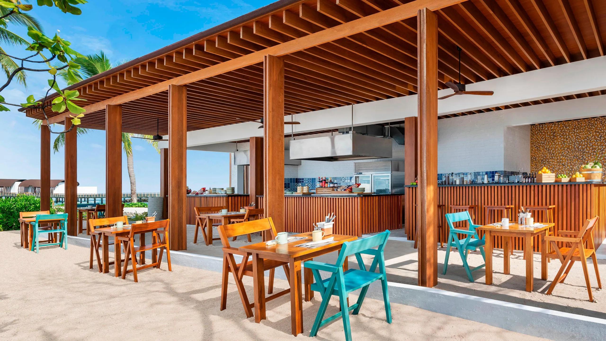 Hawker's sandy terrace set with wooden tables and teal chairs under a timber pergola