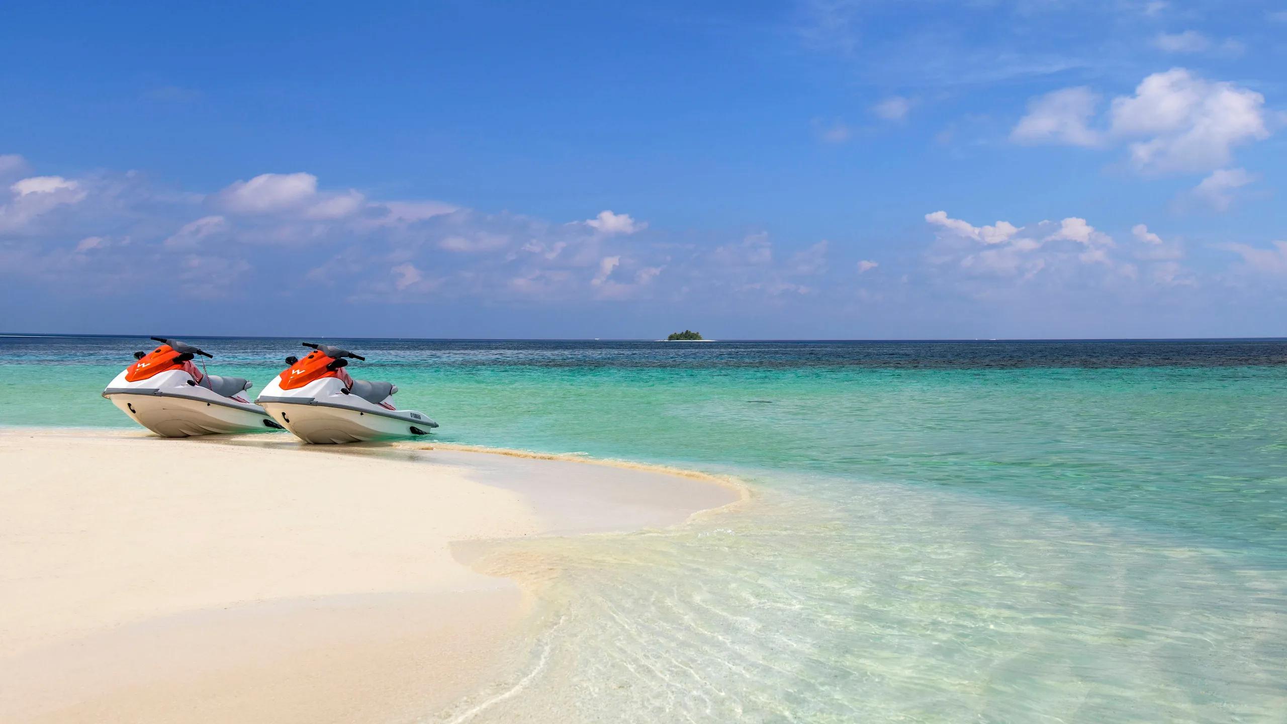 Two W-branded jet skis pulled up on a sandbank near W Maldives, with a small island visible on the horizon