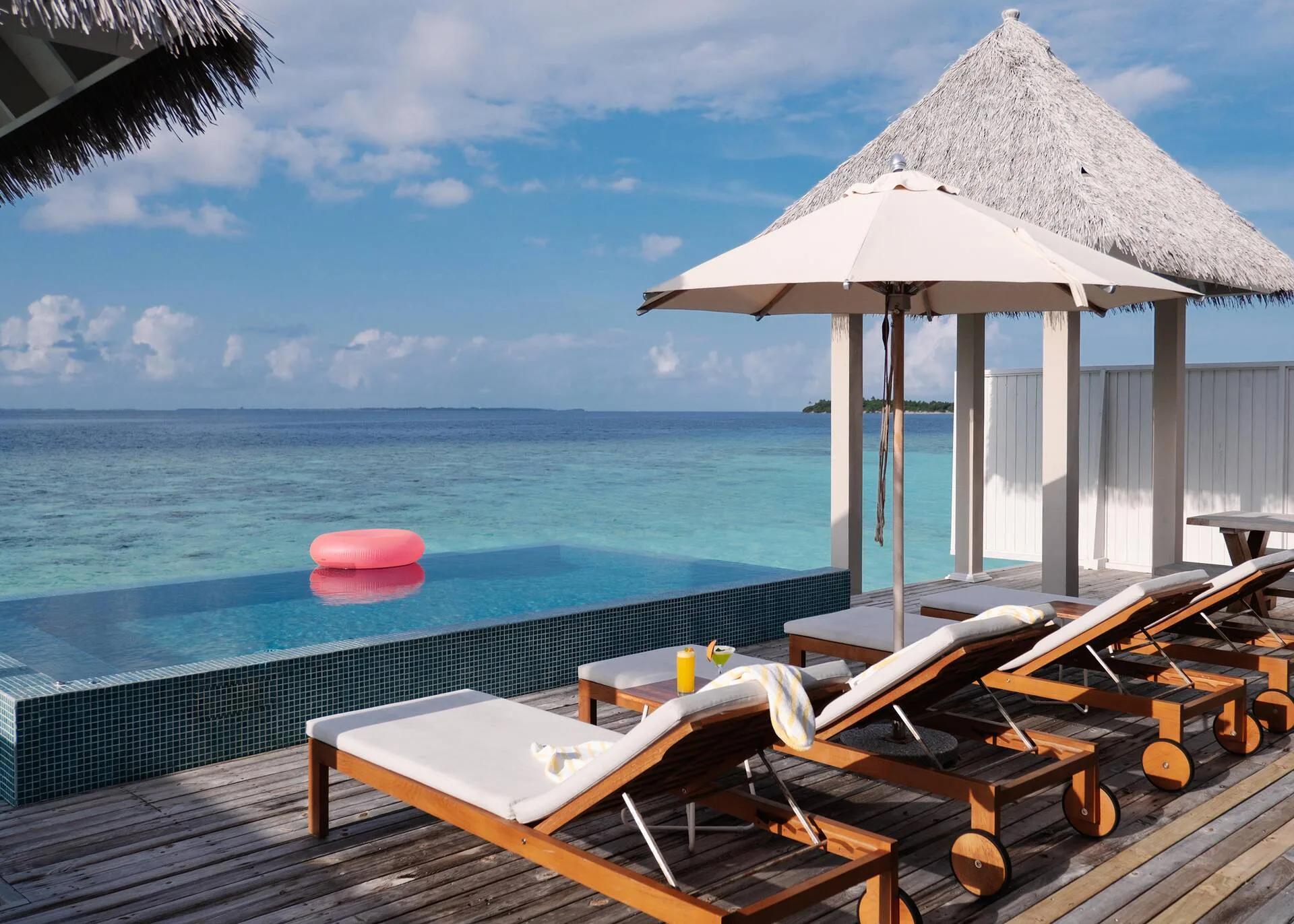 An infinity plunge pool deck under a thatched pavilion at The Standard Residence, sun loungers set beside the water and a small island visible on the horizon