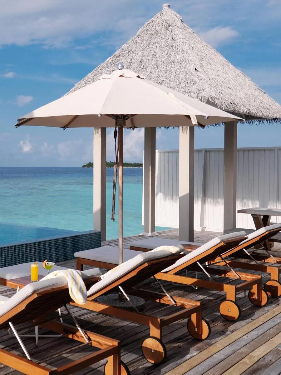 An infinity plunge pool deck under a thatched pavilion at The Standard Residence, sun loungers set beside the water and a small island visible on the horizon
