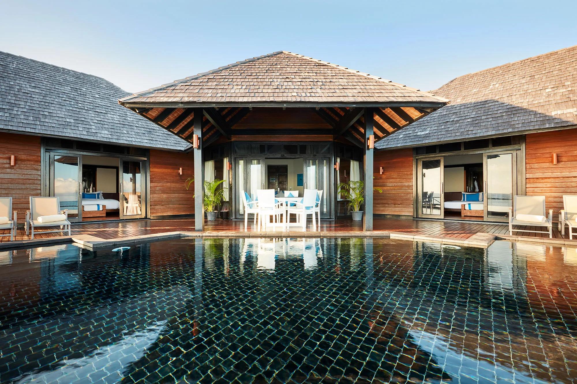 Twin bedroom pavilions of an Aqua Retreat villa facing each other across a shared black-tiled pool and open-air dining deck