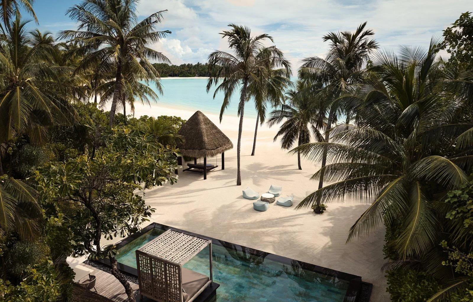 An elevated view through palm trees of a Grand Villa at One&Only Reethi Rah, a pool and beach loungers facing the lagoon