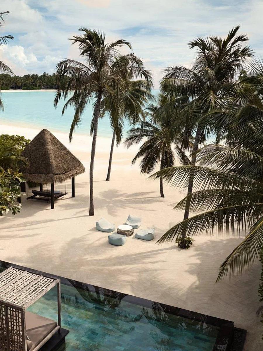 An elevated view through palm trees of a Grand Villa at One&Only Reethi Rah, a pool and beach loungers facing the lagoon