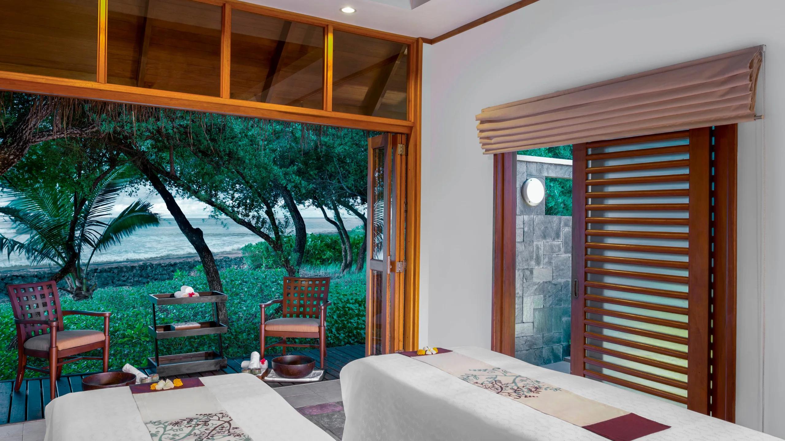 A Shine Spa treatment room with two beds and doors opening directly onto a stretch of beach and trees