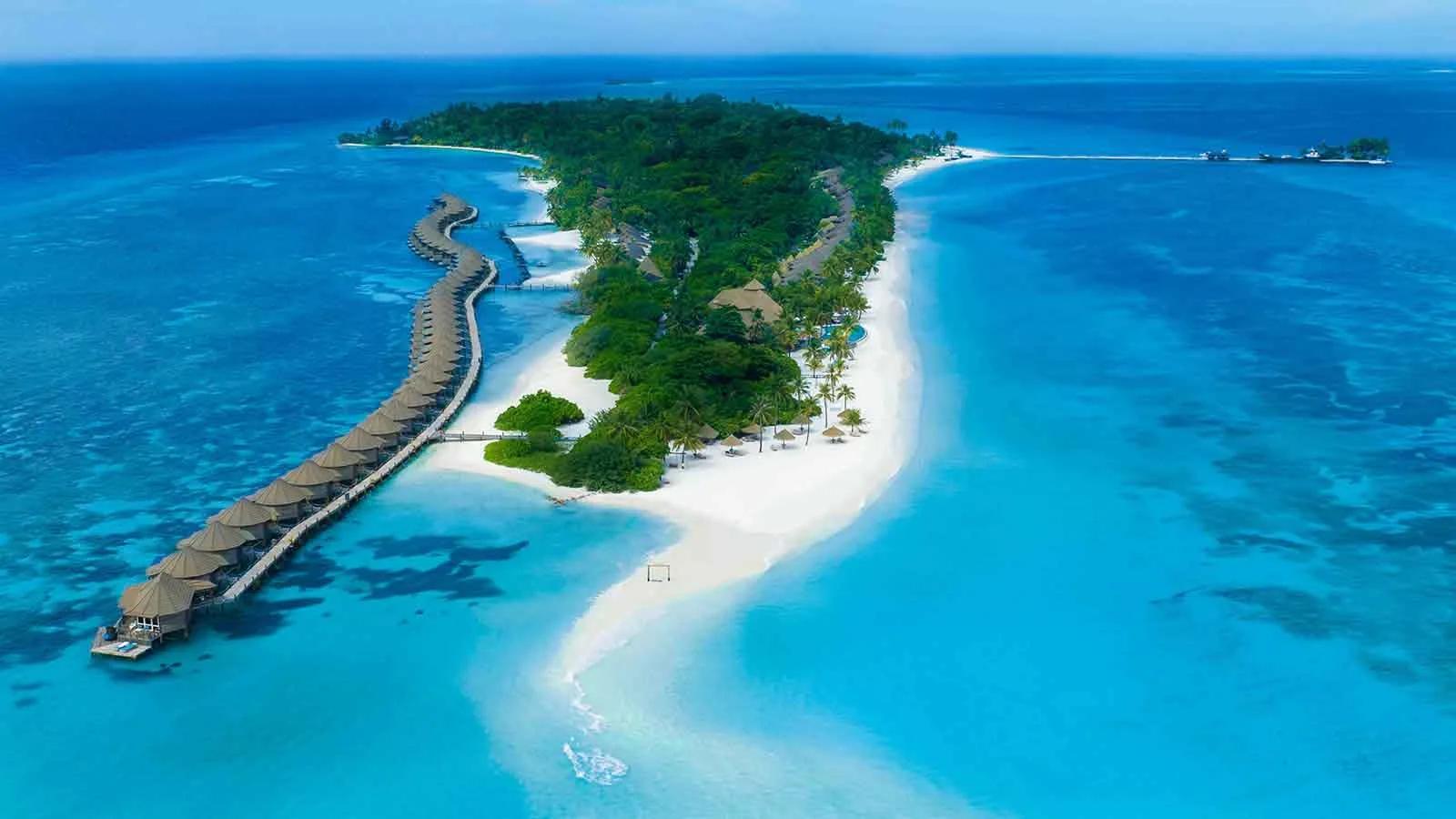 Aerial view of Kuredu island, Lhaviyani Atoll, its overwater villa jetty curving out from a tree-covered island ringed by white sand