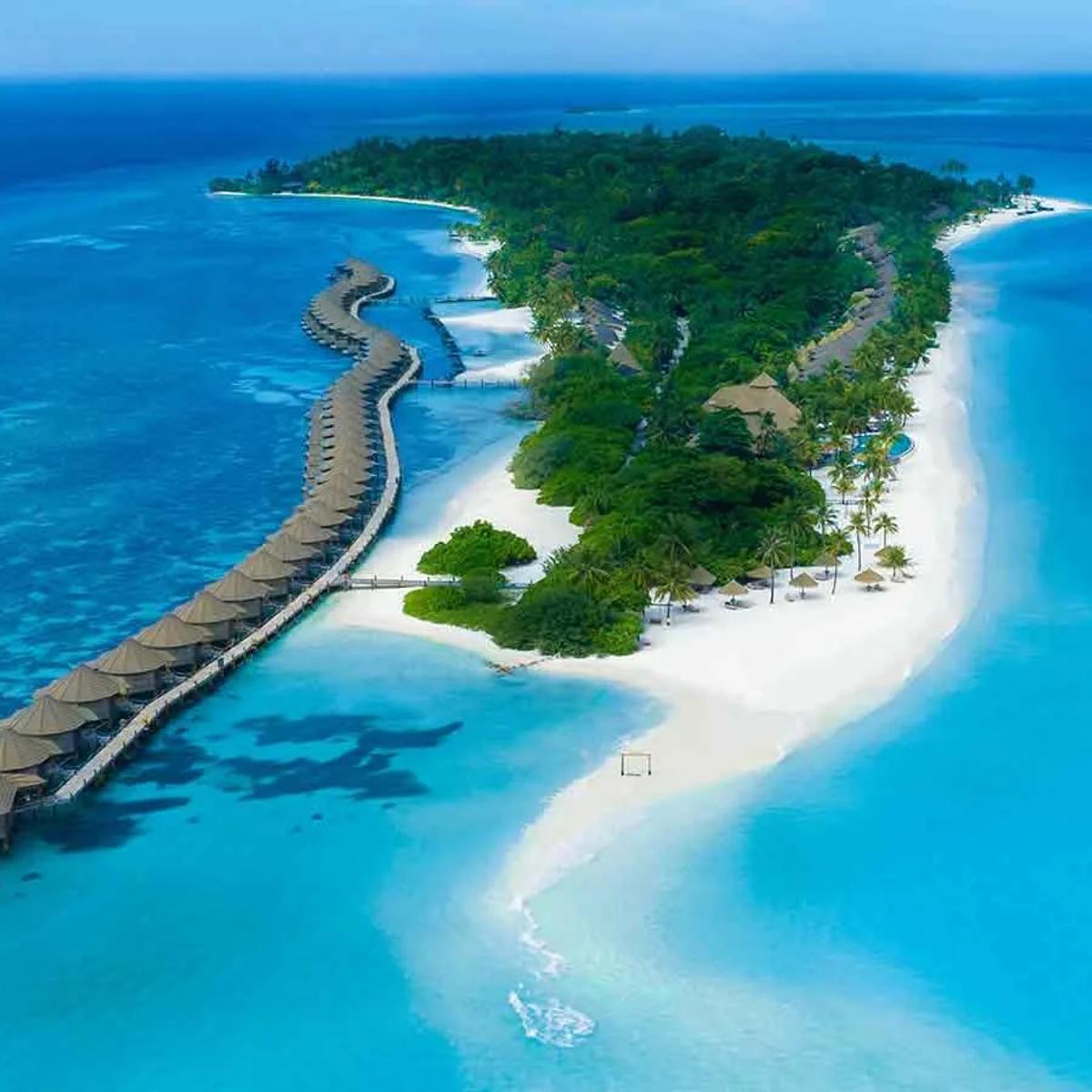 Aerial view of Kuredu island, Lhaviyani Atoll, its overwater villa jetty curving out from a tree-covered island ringed by white sand