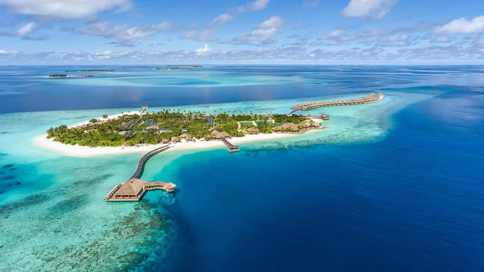 Aerial view of Hurawalhi island with the 5.8 Undersea Restaurant's jetty in the foreground and the overwater villa row curving along the reef