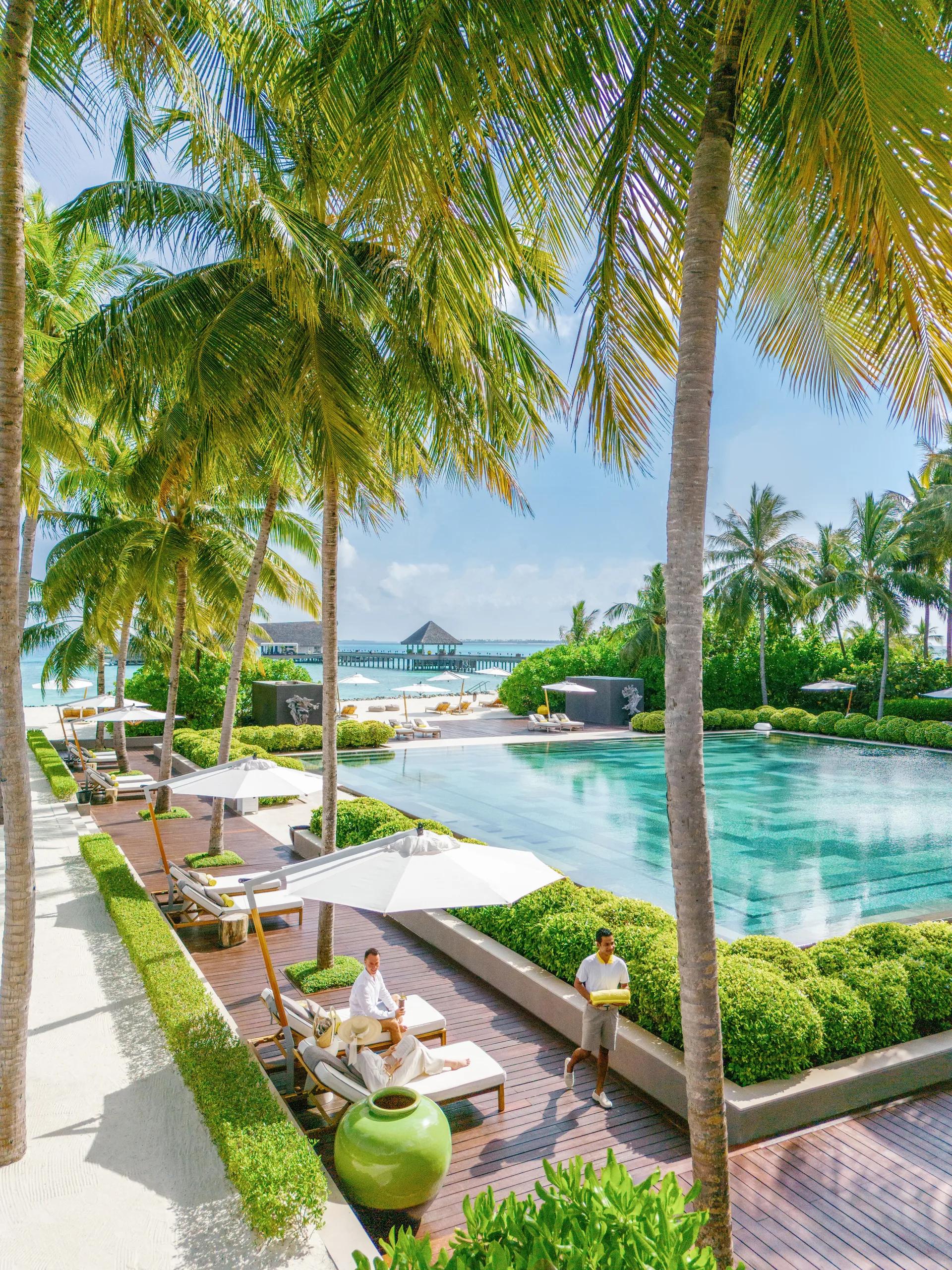 A poolside terrace open to the ocean at Cheval Blanc Randheli, palm trees framing loungers and the lagoon beyond