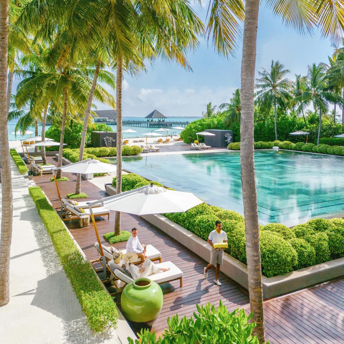 A poolside terrace open to the ocean at Cheval Blanc Randheli, palm trees framing loungers and the lagoon beyond