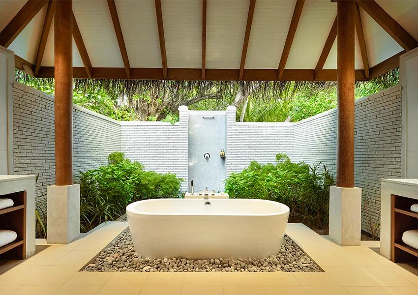 A Deluxe Villa's open-air garden bathroom, a freestanding tub set among tropical planting beneath a thatched roof