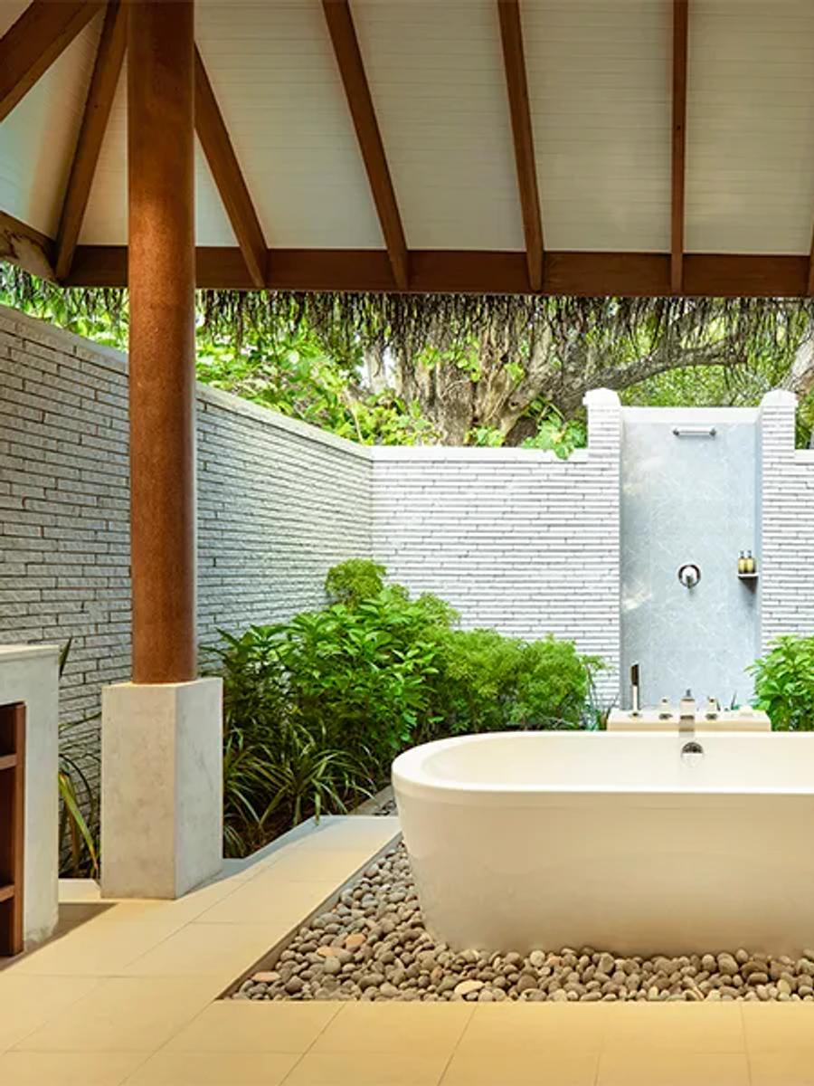 A Deluxe Villa's open-air garden bathroom, a freestanding tub set among tropical planting beneath a thatched roof