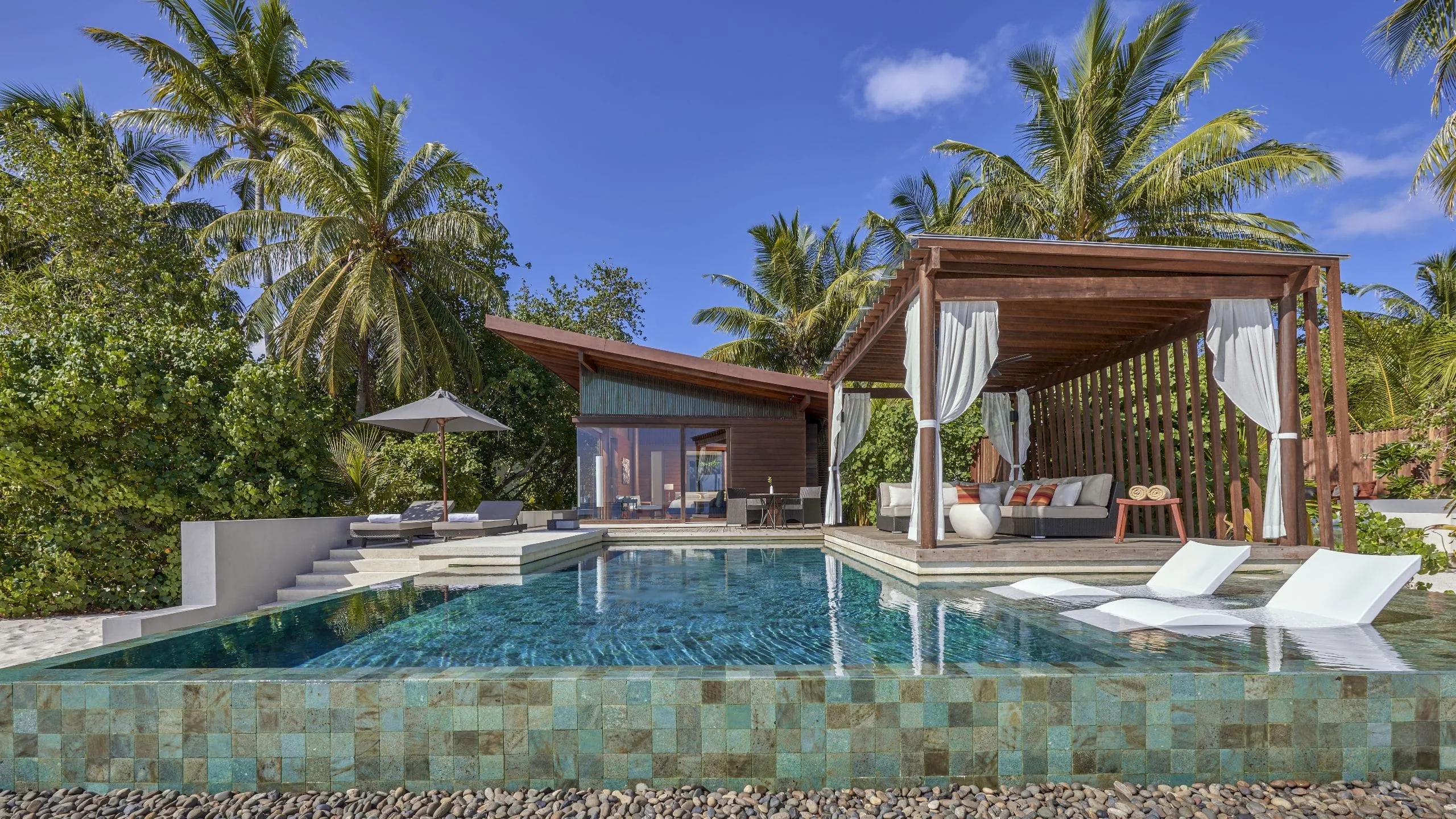 The private plunge pool and curtained outdoor cabana of a Deluxe Beach Pool Villa, framed by palm trees