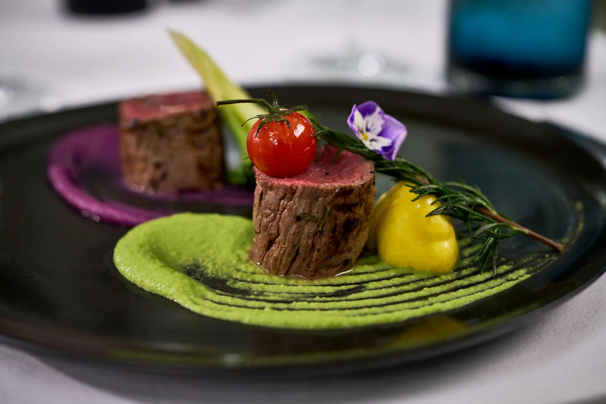 A plated tasting course at Culinarium — seared beef, pea purée and beet purée, garnished with a cherry tomato and edible flower