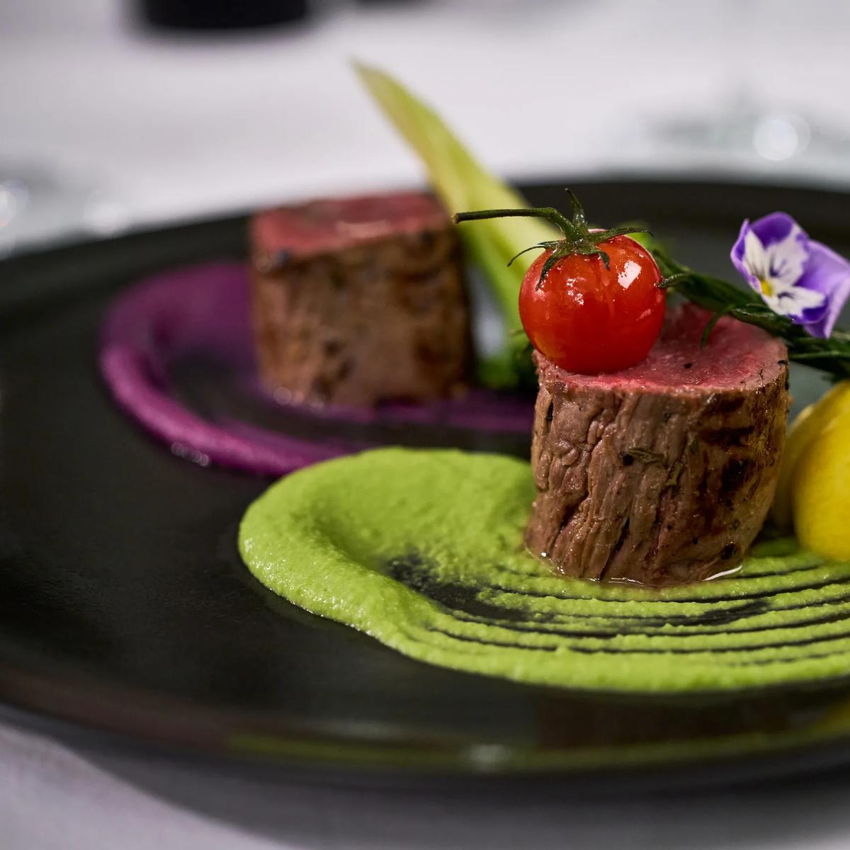 A plated tasting course at Culinarium — seared beef, pea purée and beet purée, garnished with a cherry tomato and edible flower