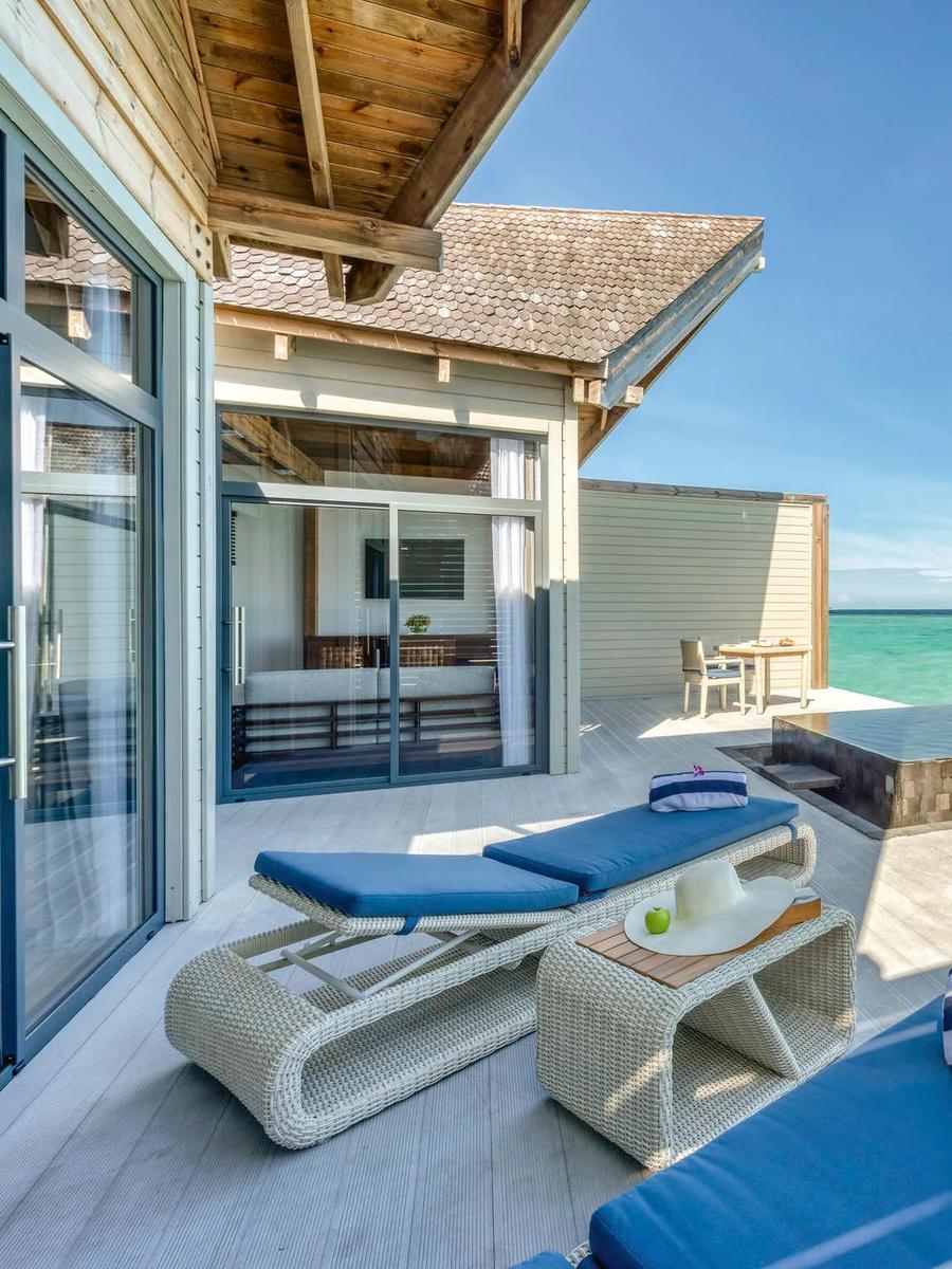 Deck of an overwater pool villa with a private pool, two blue sun loungers and a sun hat, open ocean stretching to the horizon