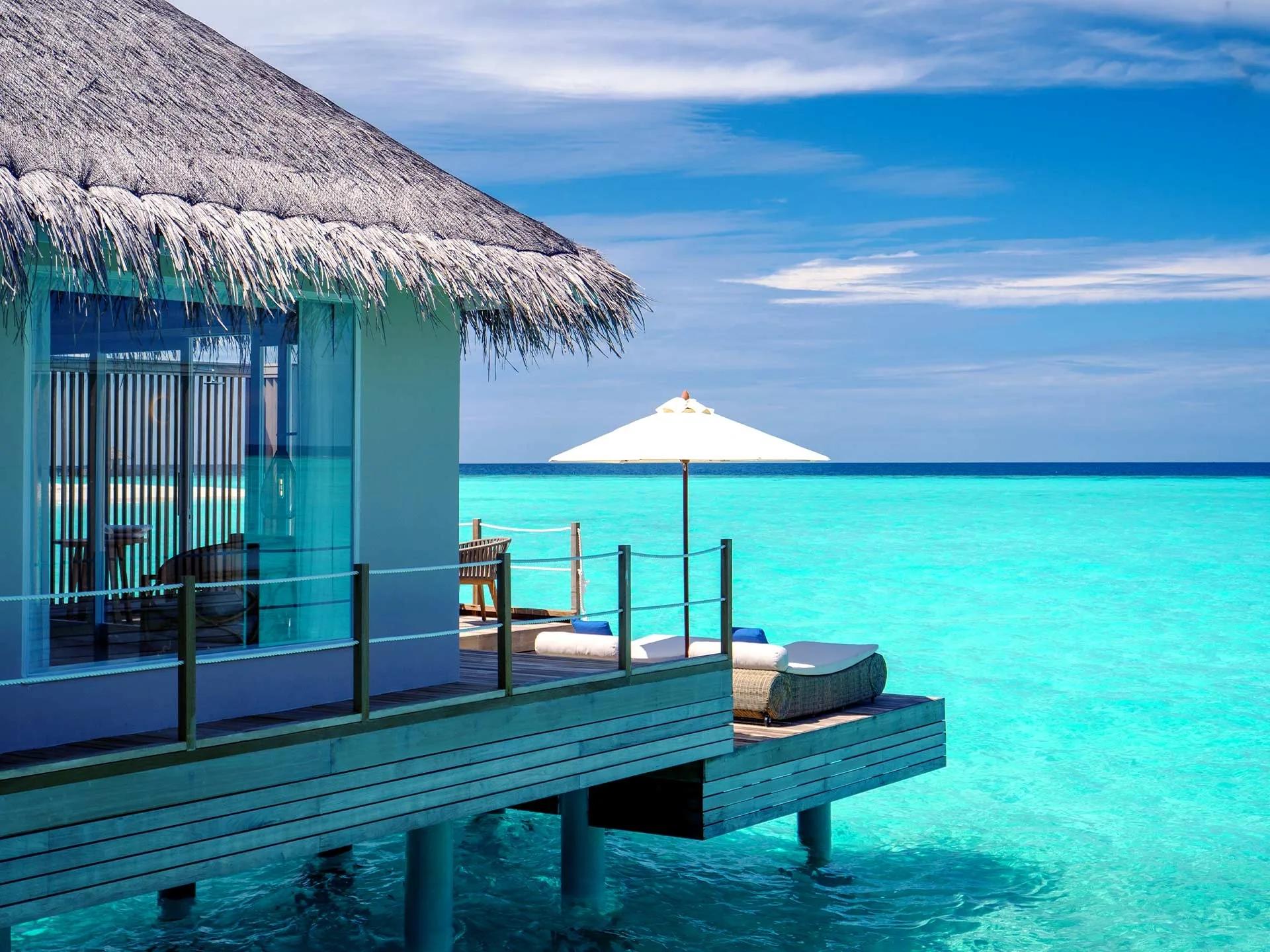 A Sunset Water Villa's overwater deck and umbrella at Baglioni Maldives, facing the open lagoon