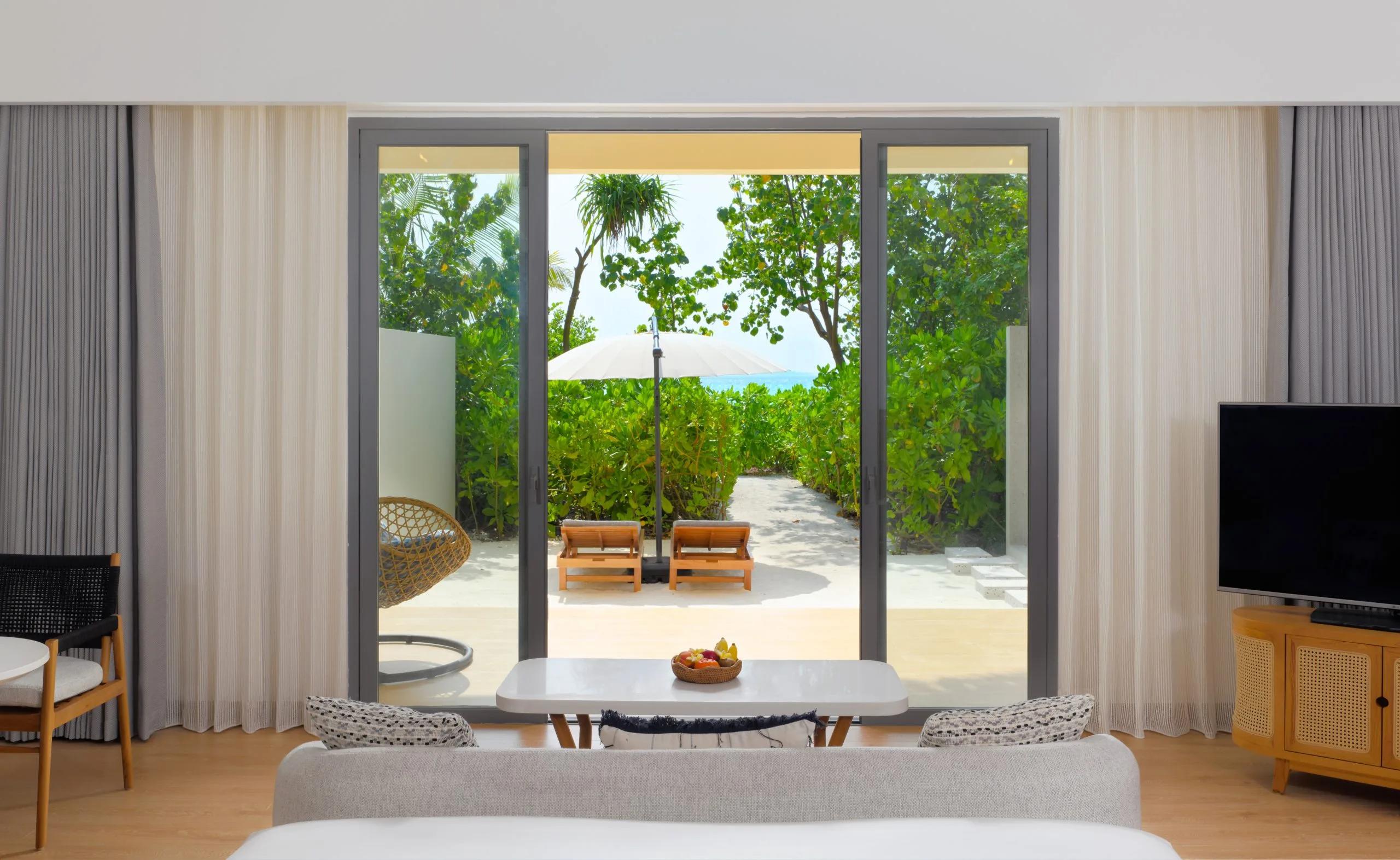A Beach Villa's bedroom opening onto its deck at dusitD2 Feydhoo Maldives