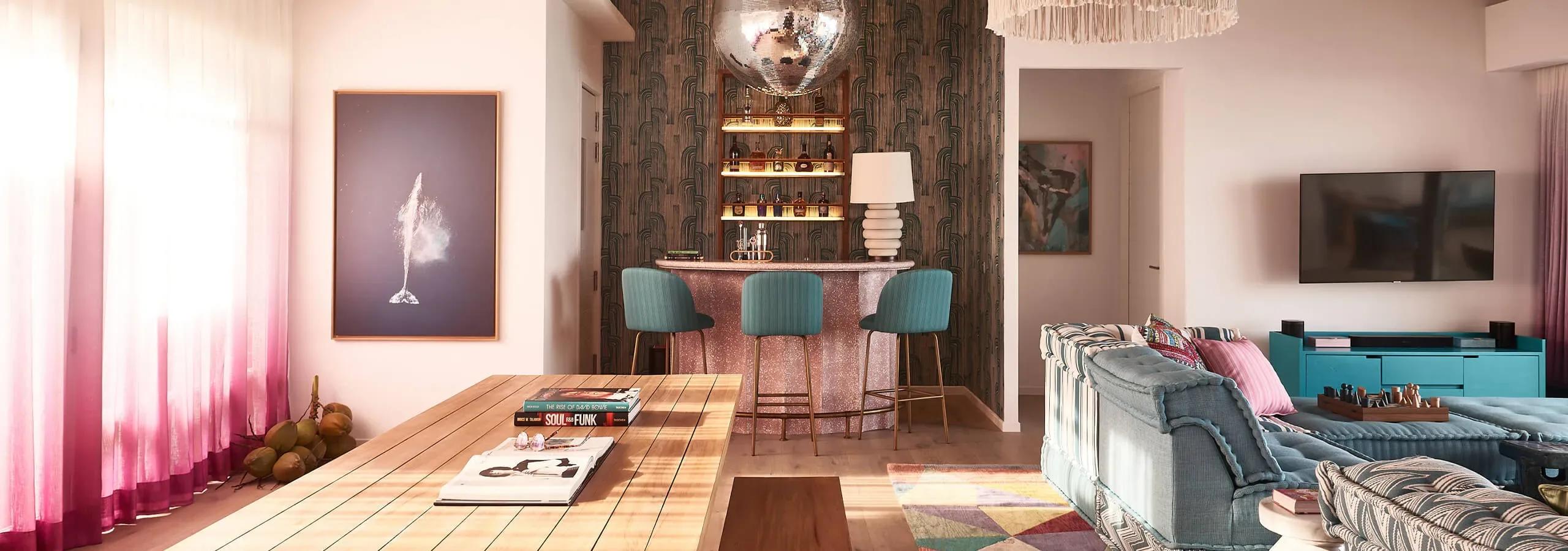 A mirrored disco ball hanging above the in-villa bar of a Two Bedroom Rockstar Villa, with teal velvet stools and a colourful striped sofa in the room beyond