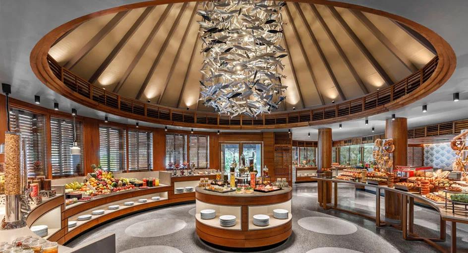 Interior of Fushi Café, Anantara Dhigu's buffet restaurant, with a circular fish-motif chandelier over the spread