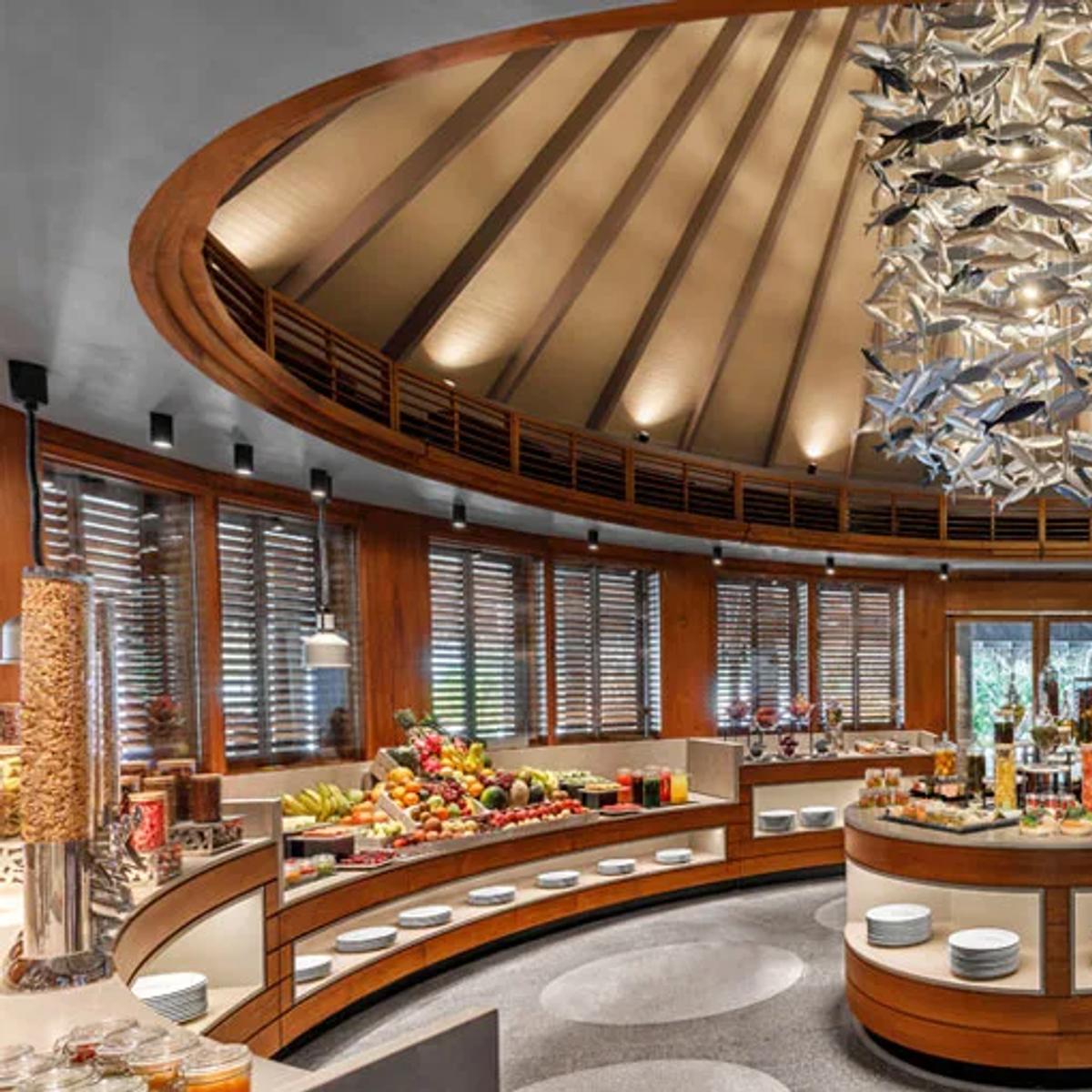 Interior of Fushi Café, Anantara Dhigu's buffet restaurant, with a circular fish-motif chandelier over the spread