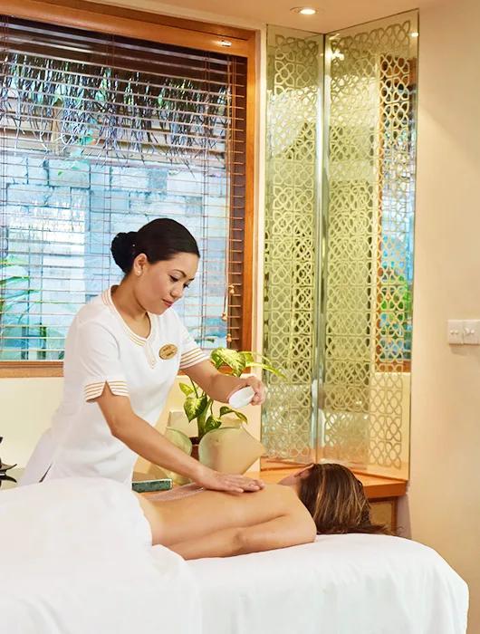 A therapist in white uniform applying a back treatment to a guest lying face-down on a spa table at Serenity Spa