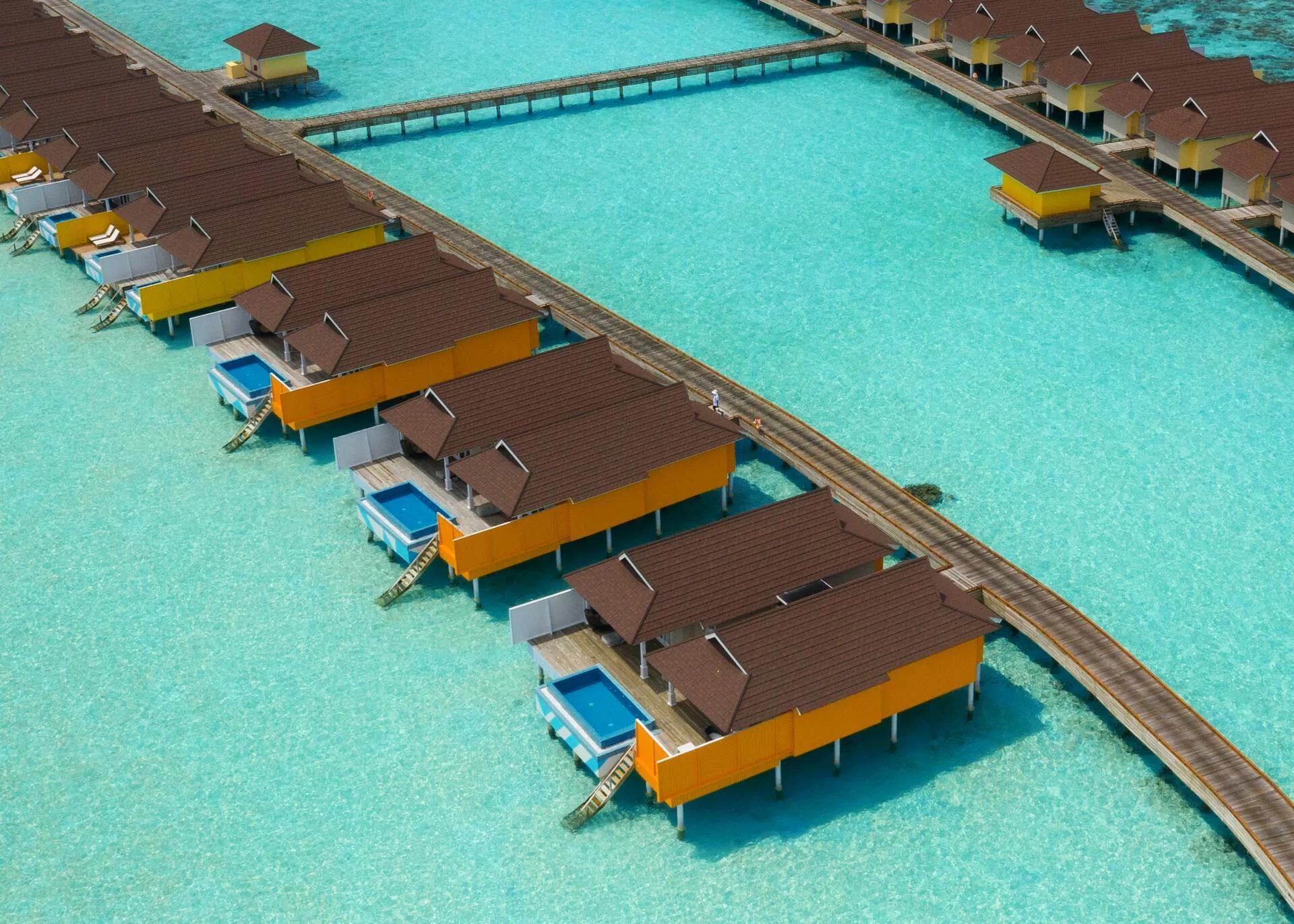 Aerial view of The Standard's orange- and yellow-panelled overwater villas along a boardwalk, private plunge pools set off each deck